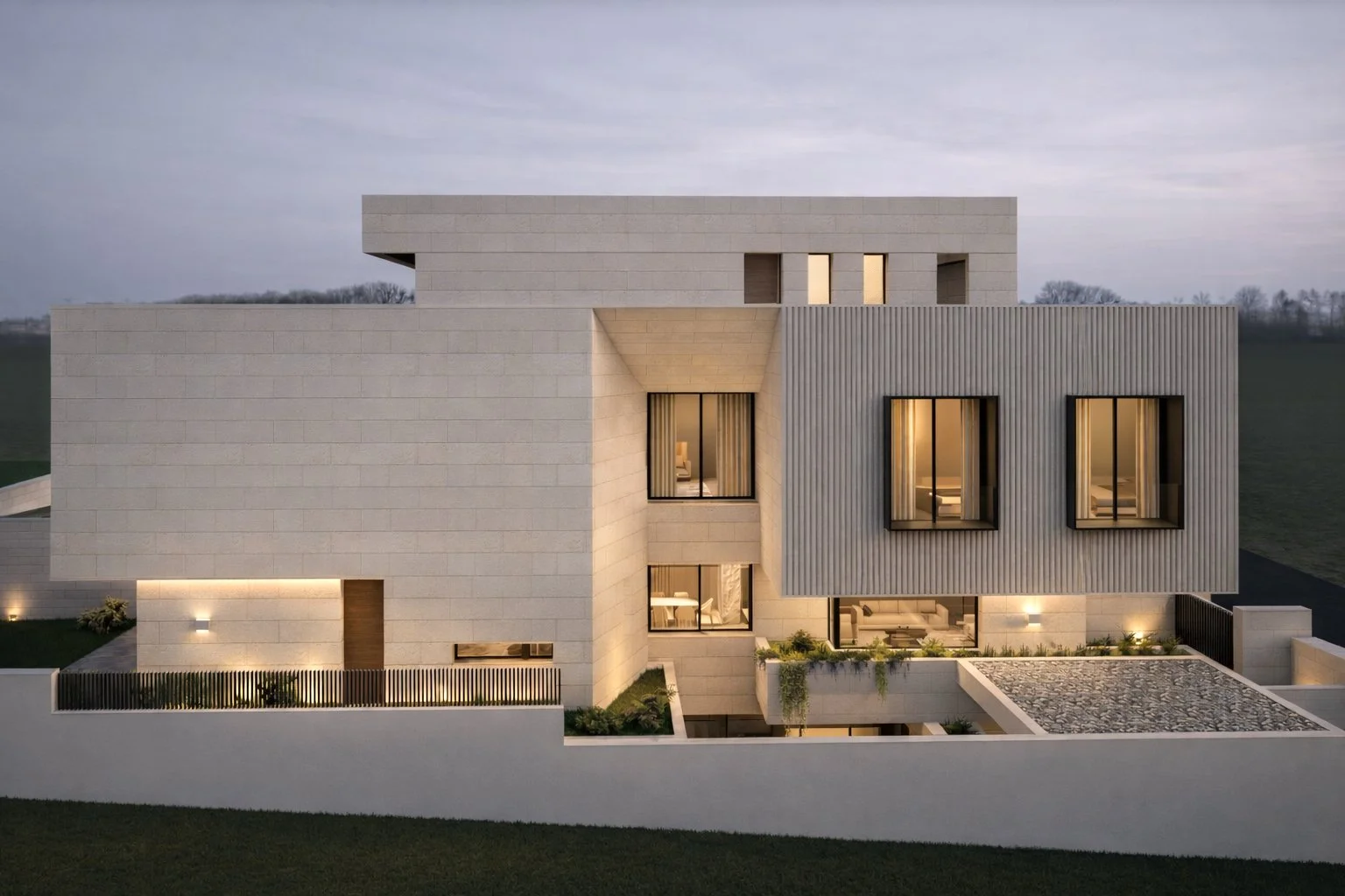 Modern multi-story house with beige brick exterior and large windows, illuminated at night, with a landscaped yard and a white fence.