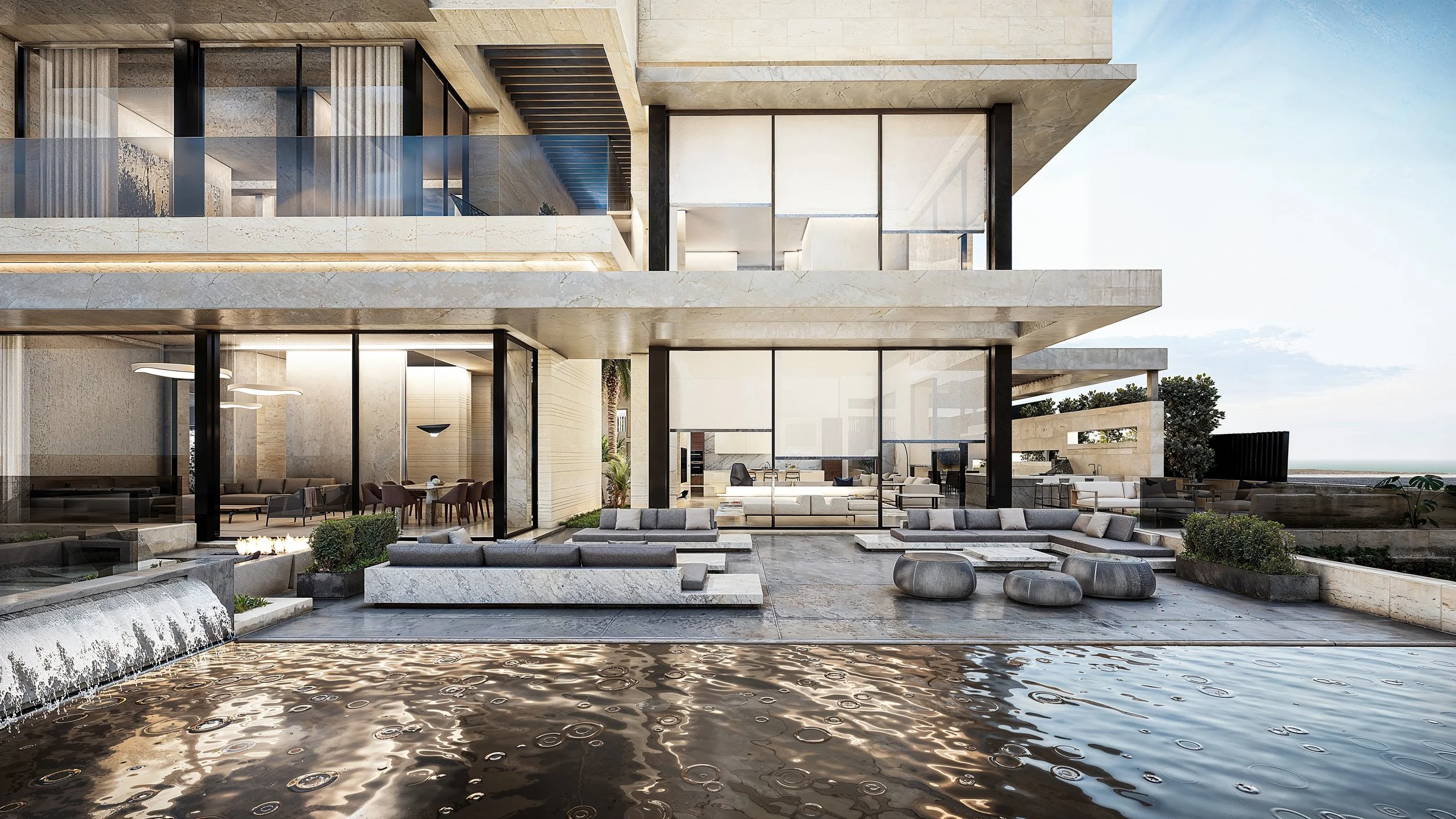 Modern multi-story house with large glass windows and outdoor seating area, overlooking a swimming pool and water feature, with a clear sky in the background.