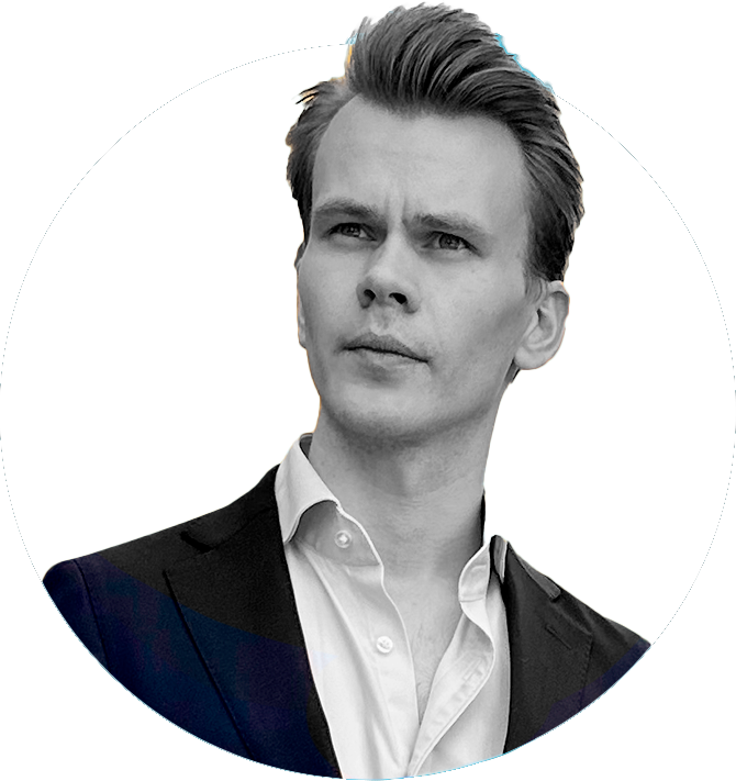 Portrett av en ung mann med lyst hår iført hvit skjorte og sort blazer, sett mot en hvit bakgrunn.