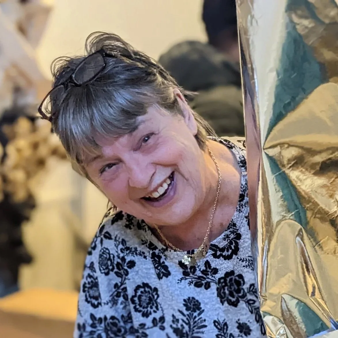A woman smiling and laughing, positioned near a table with gold-colored balloons or decorations.
