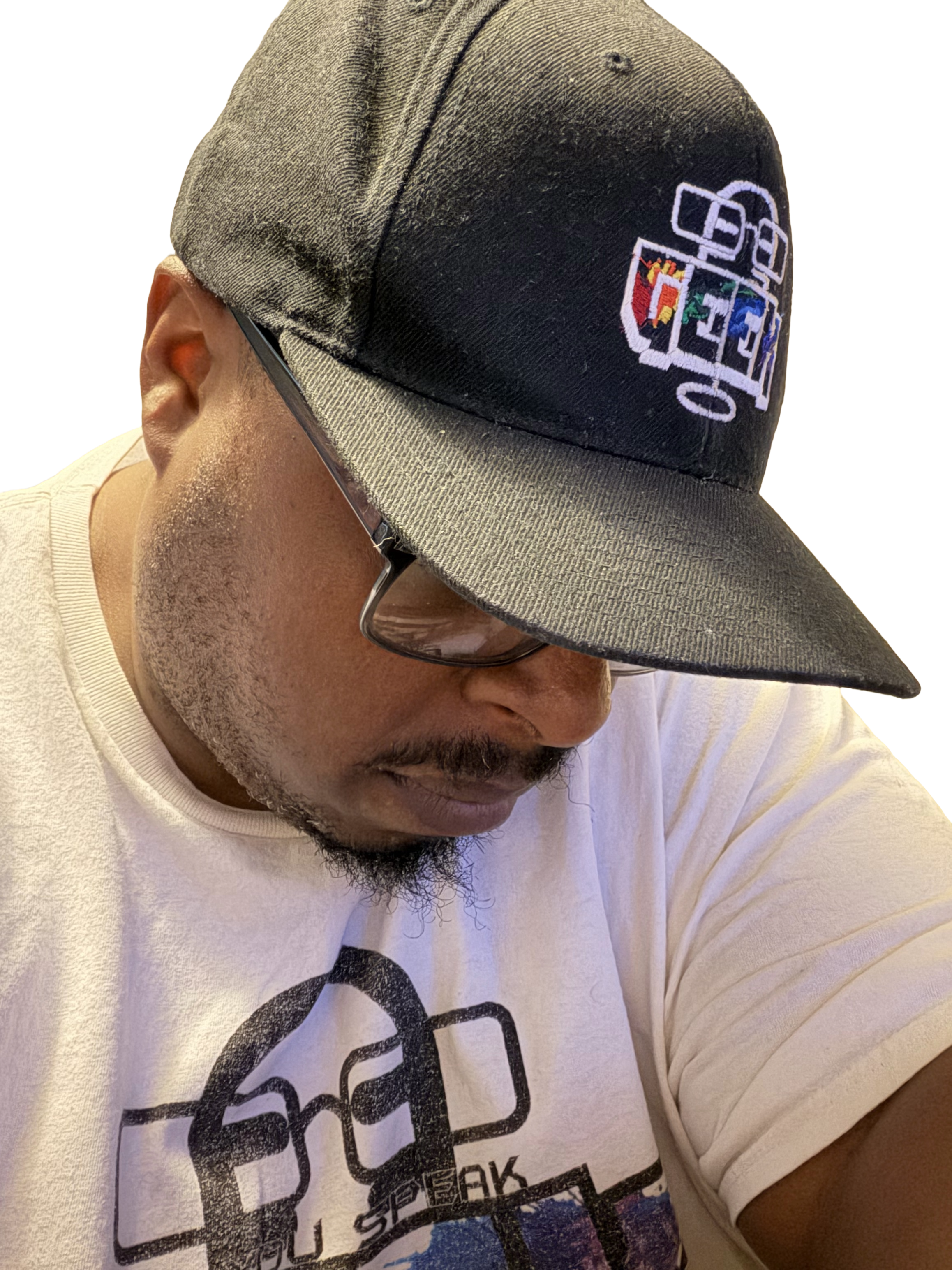 A man wearing a black and beige snapback cap with a colorful embroidered logo, a white T-shirt with black text and a graphic, and glasses, is looking downward.