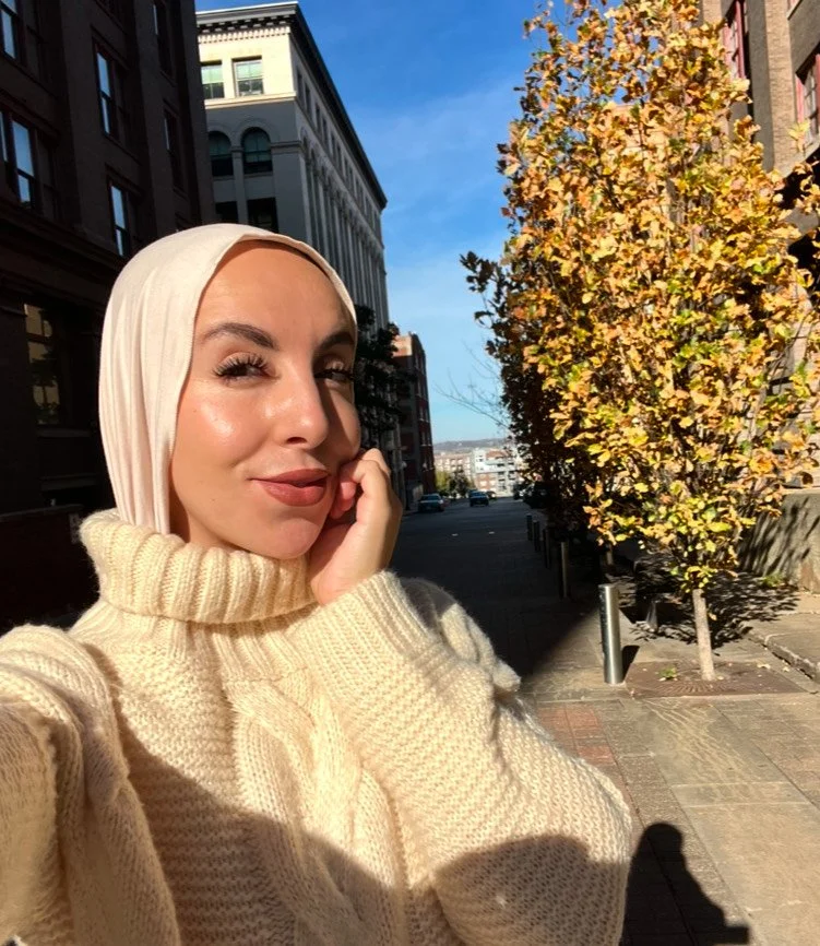 Woman in a hijab taking a selfie on a sunny urban street.