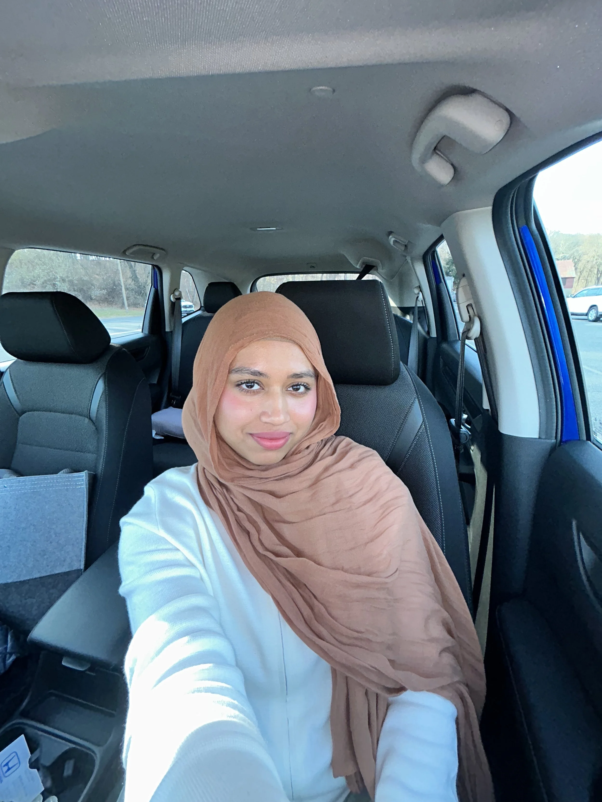 Person wearing a brown hijab sitting inside a car.