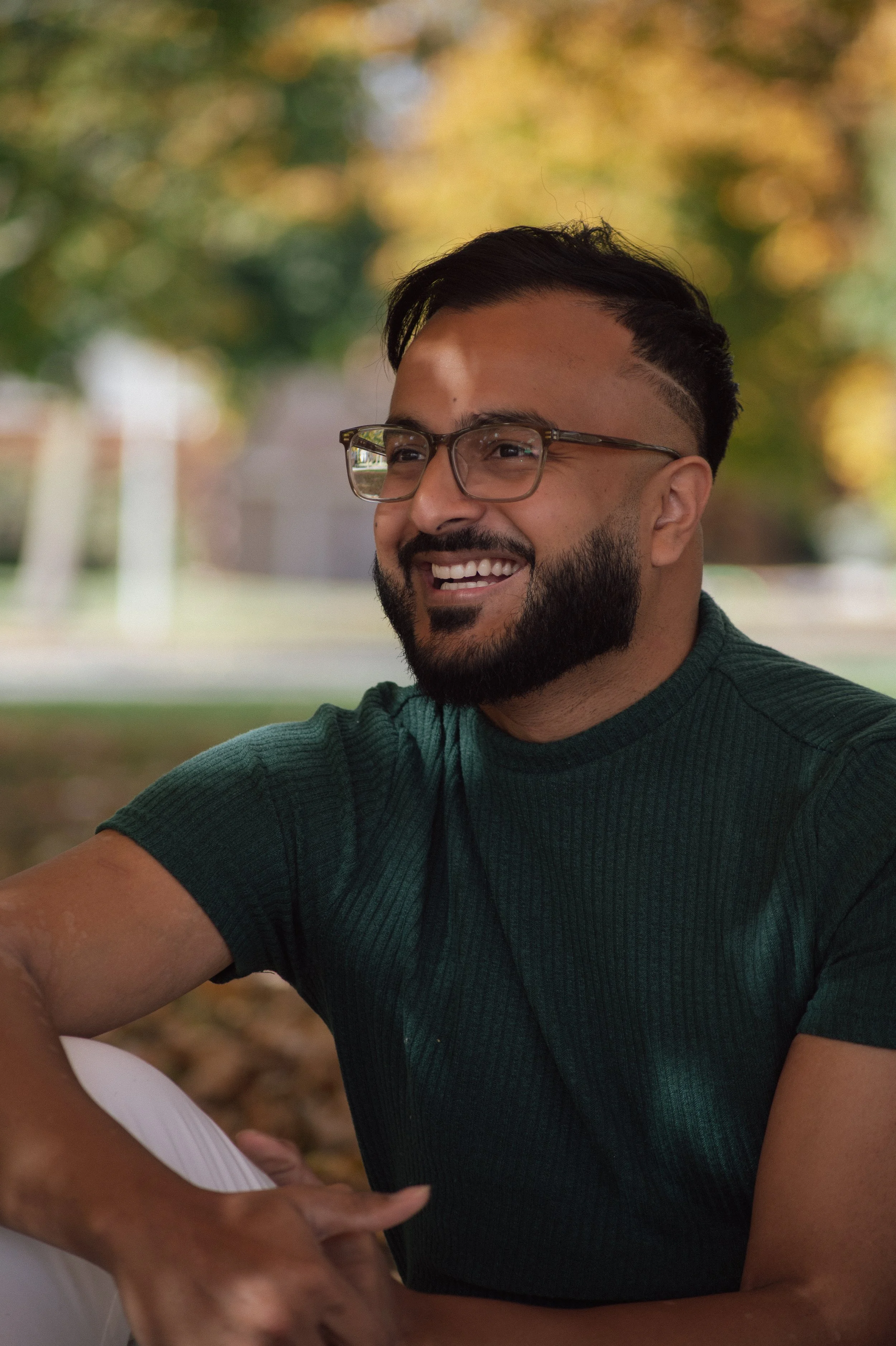 Smiling person wearing glasses and a green t-shirt outdoors in a park during fall.