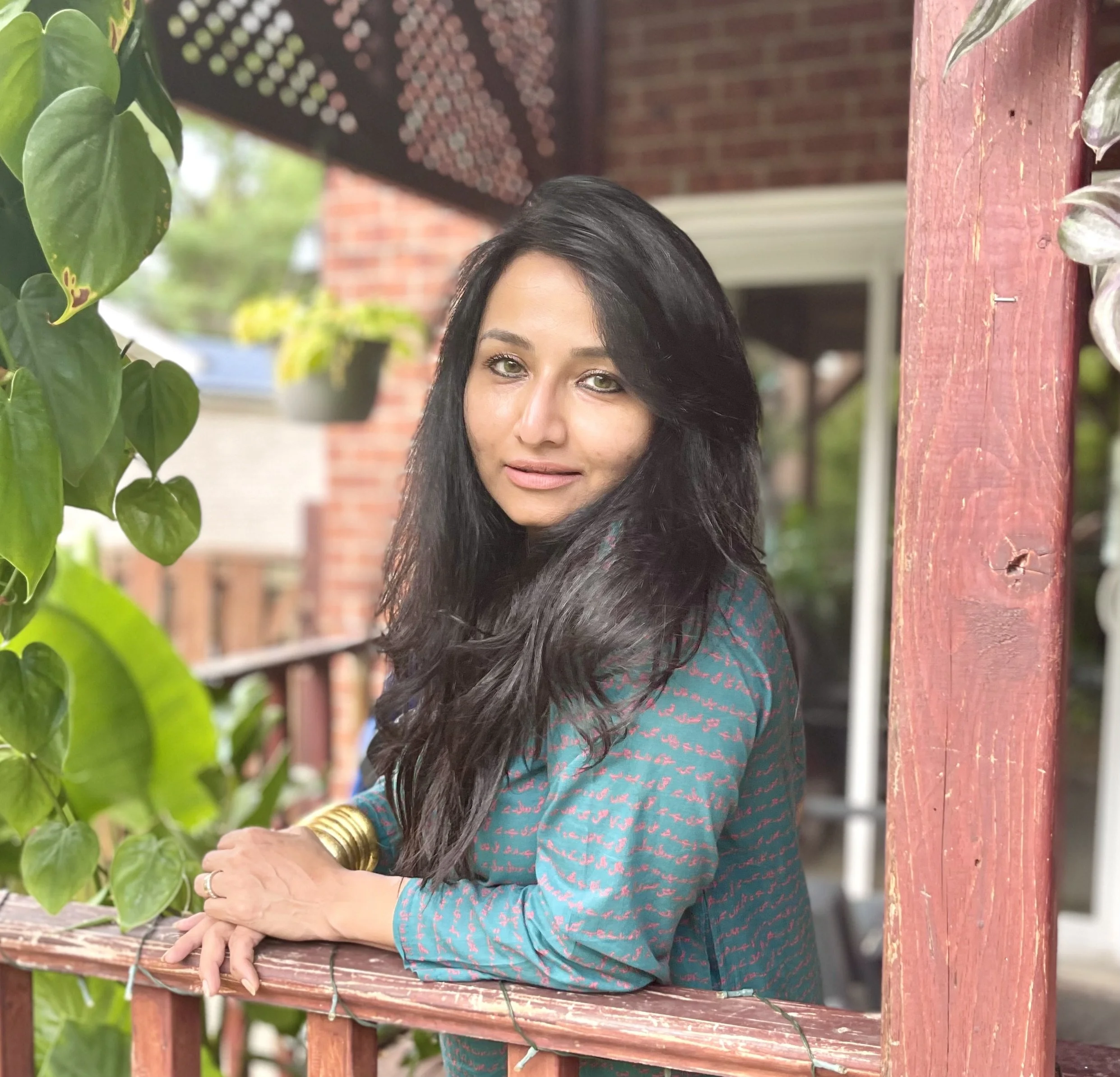 Woman leaning on wooden railing in outdoor setting with plants.