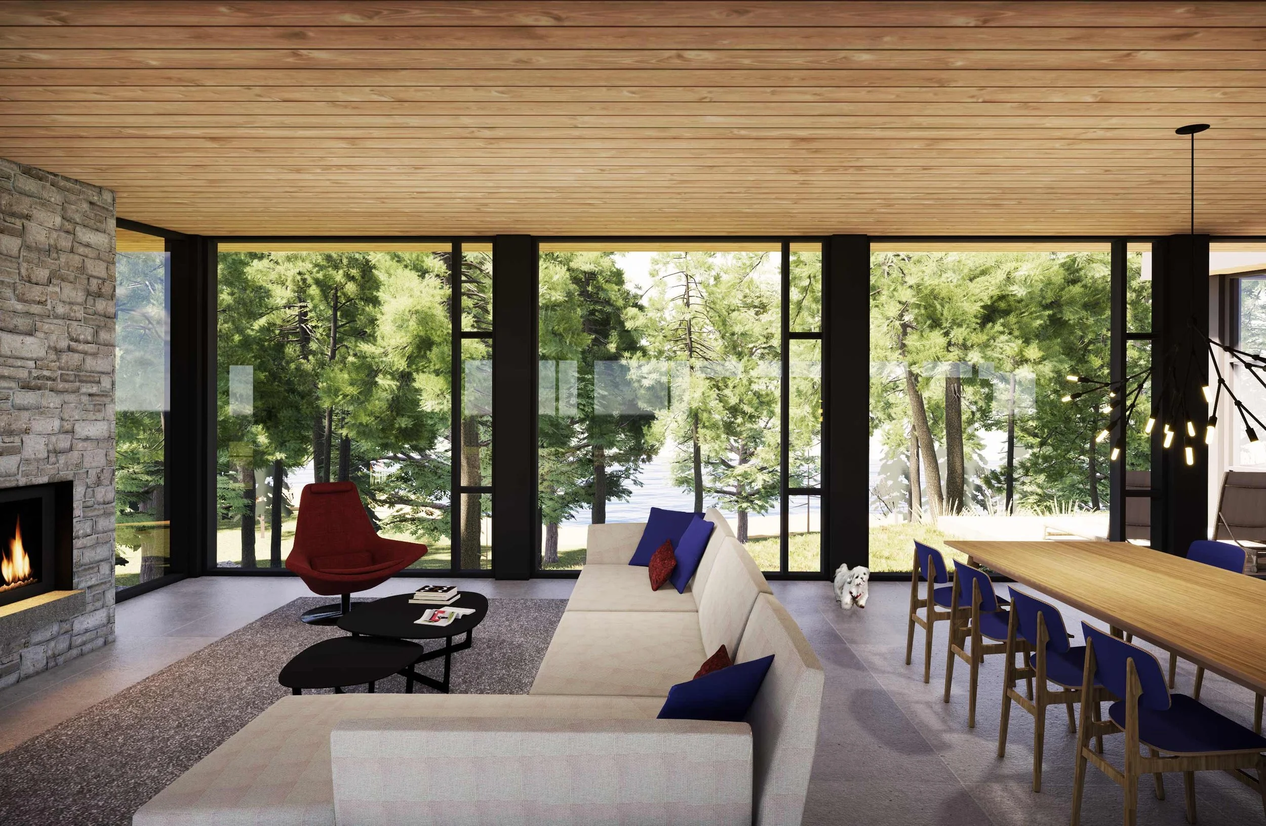Modern living room with large floor-to-ceiling windows overlooking trees, a stone fireplace, a white sofa with colorful pillows, a red lounge chair, a small black coffee table, a dining table with blue chairs, and a dog near the window.