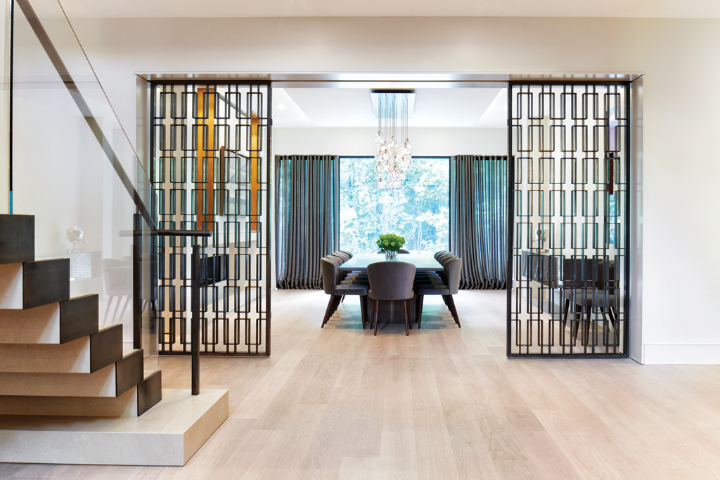 A modern, open-concept dining area with a glass table, six chairs, large windows with curtains, a chandelier, and black decorative room dividers.
