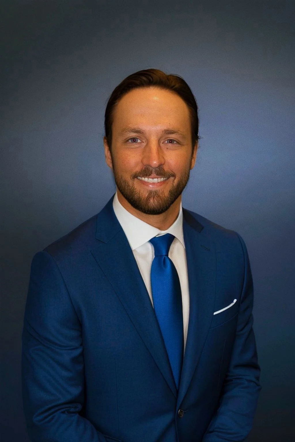 A man in a blue suit and tie smiling against a blue background.