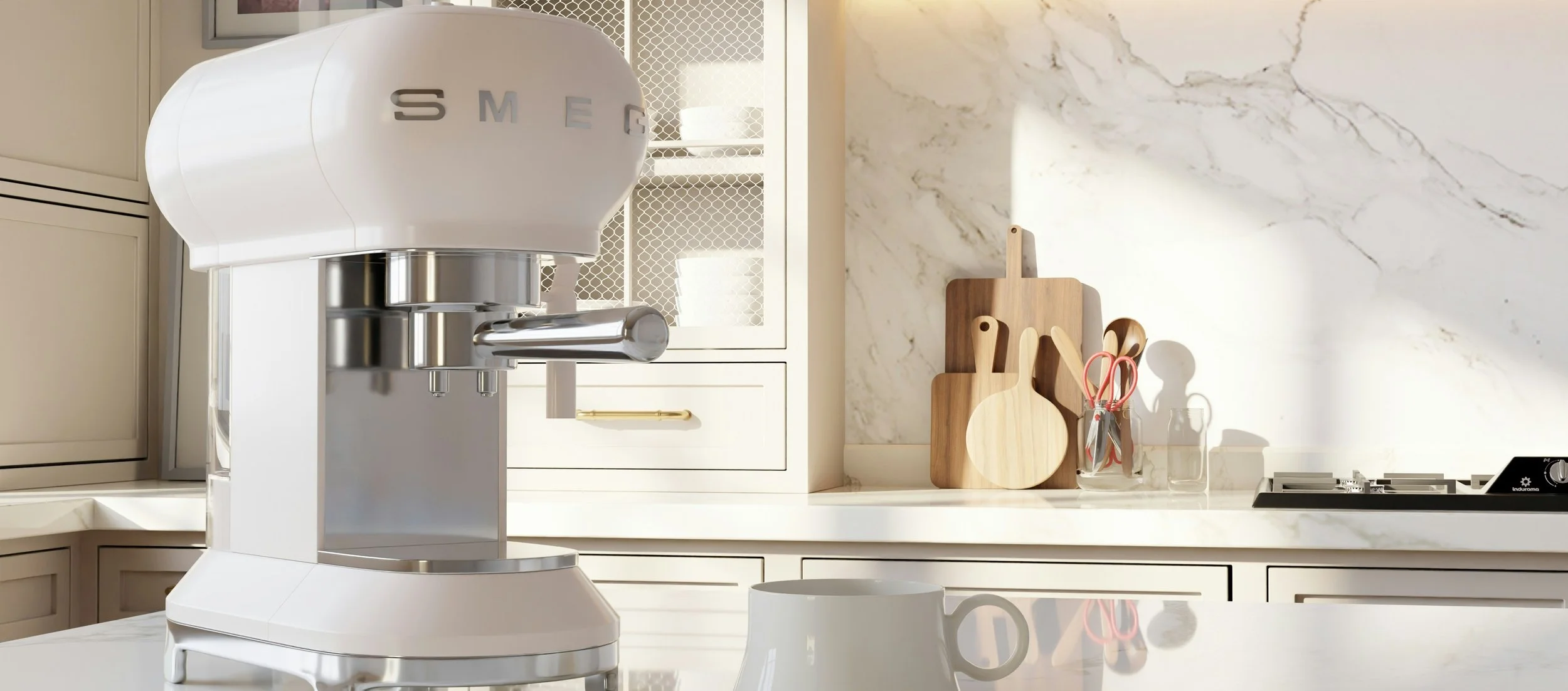 Modern kitchen with a white Smeg espresso machine on a marble countertop, wooden cutting boards, scissors, a glass jar, and a white mug in front, cream-colored cabinets, and a gas stove.