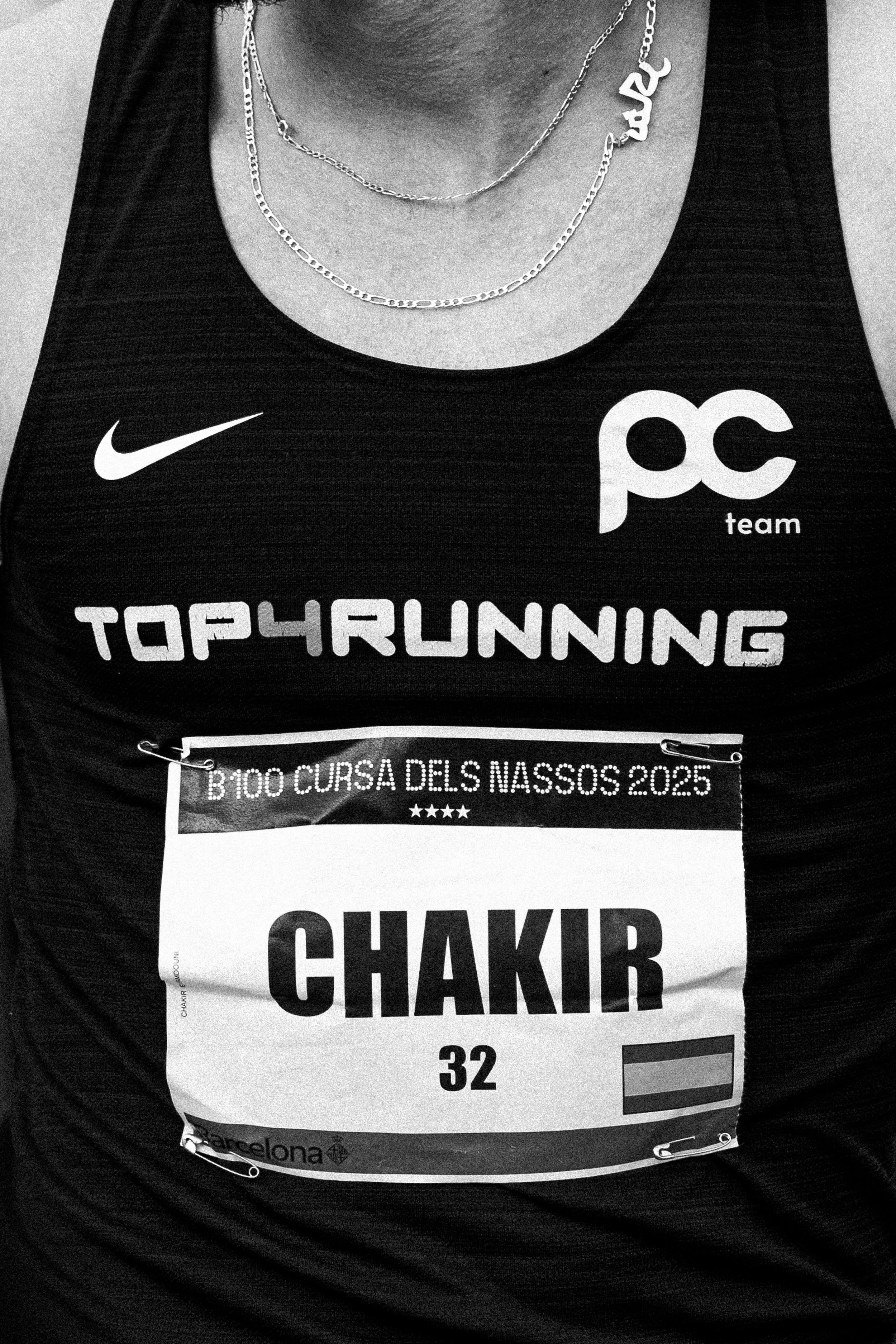 Número de corredor y detalles del evento en un dorsal de carrera, que dice 'B 100 Cursa dels Nassos 2025, CHAKIR 32' en una camiseta de corredor en un evento de atletismo en Barcelona.