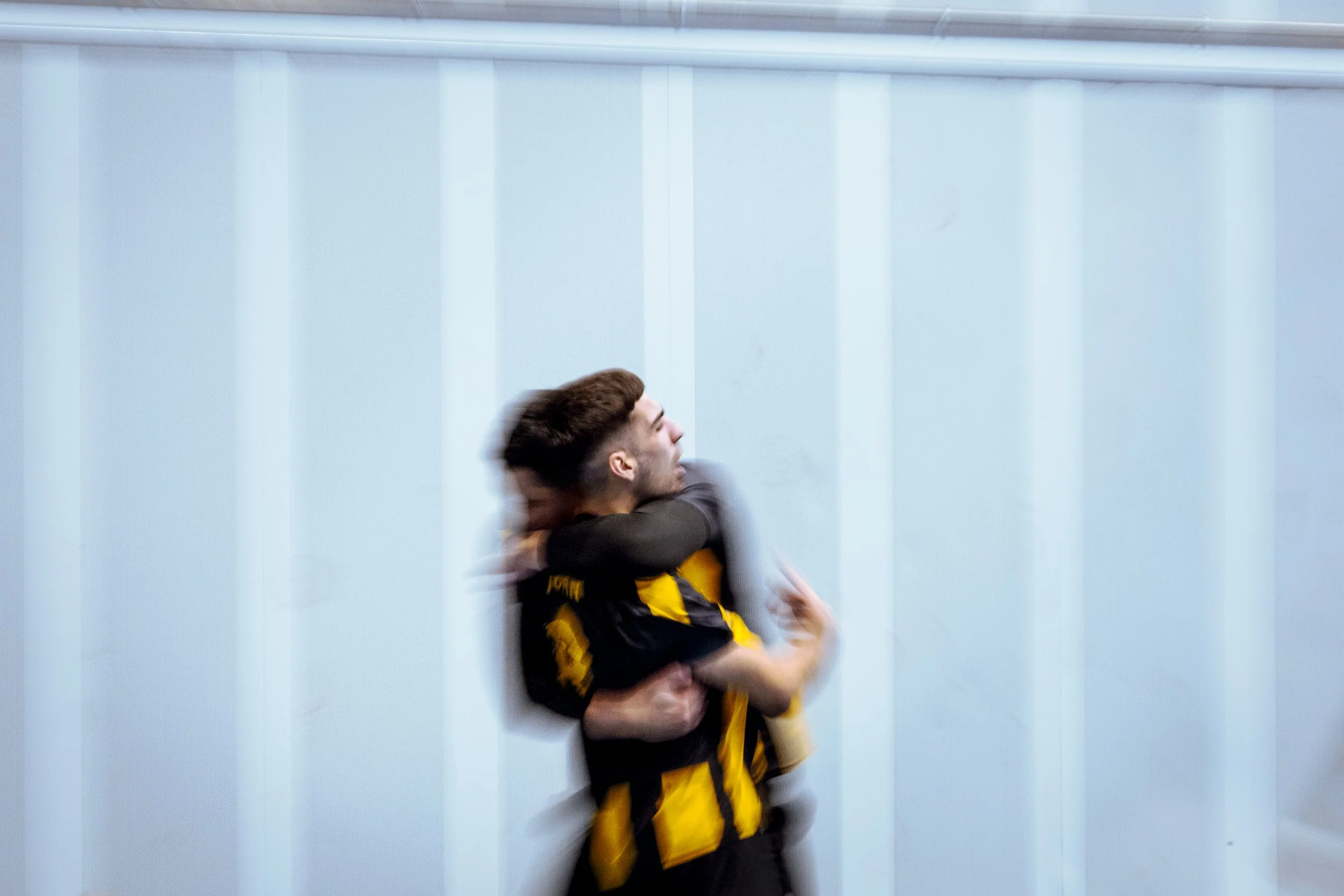 Dos futbolistas se abrazan en un estadio, uno con uniforme amarillo y negro.