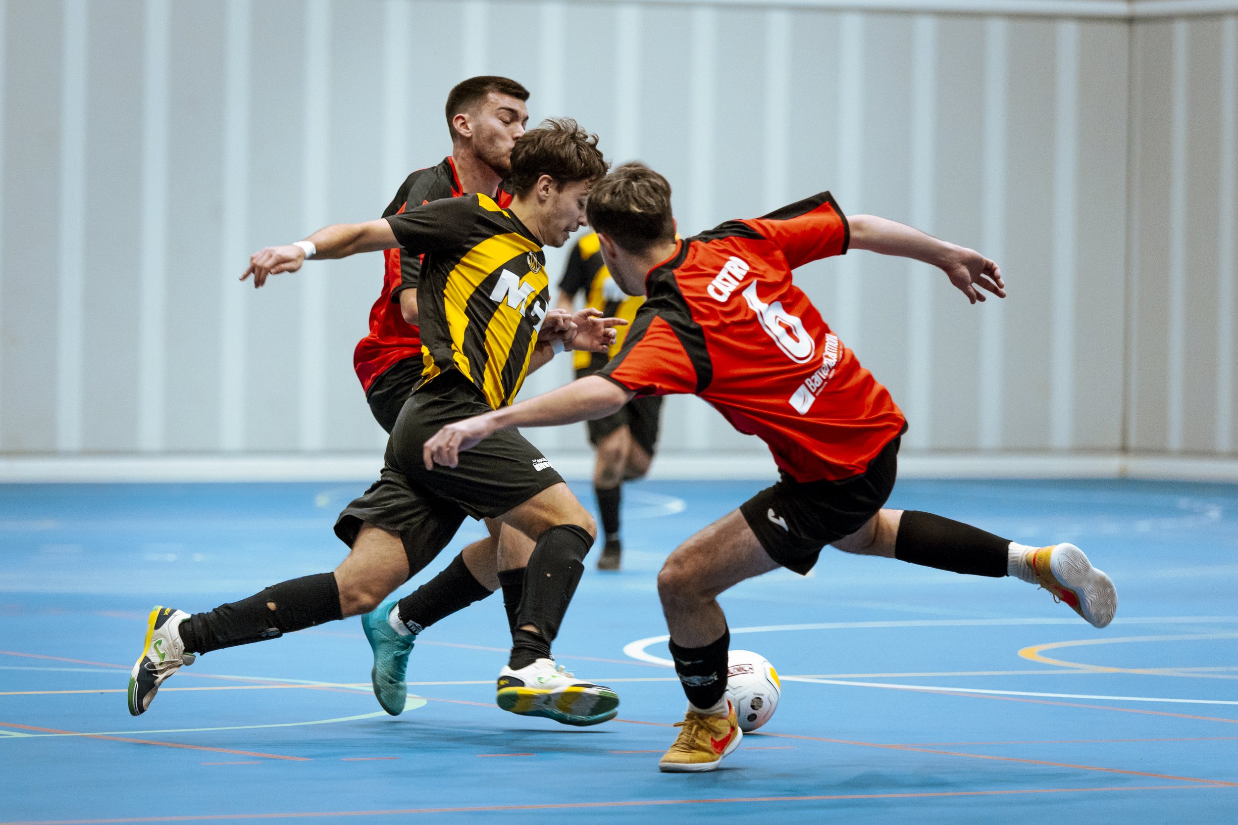 Jugadores de fútbol sala en una cancha indoor luchando por el balón.