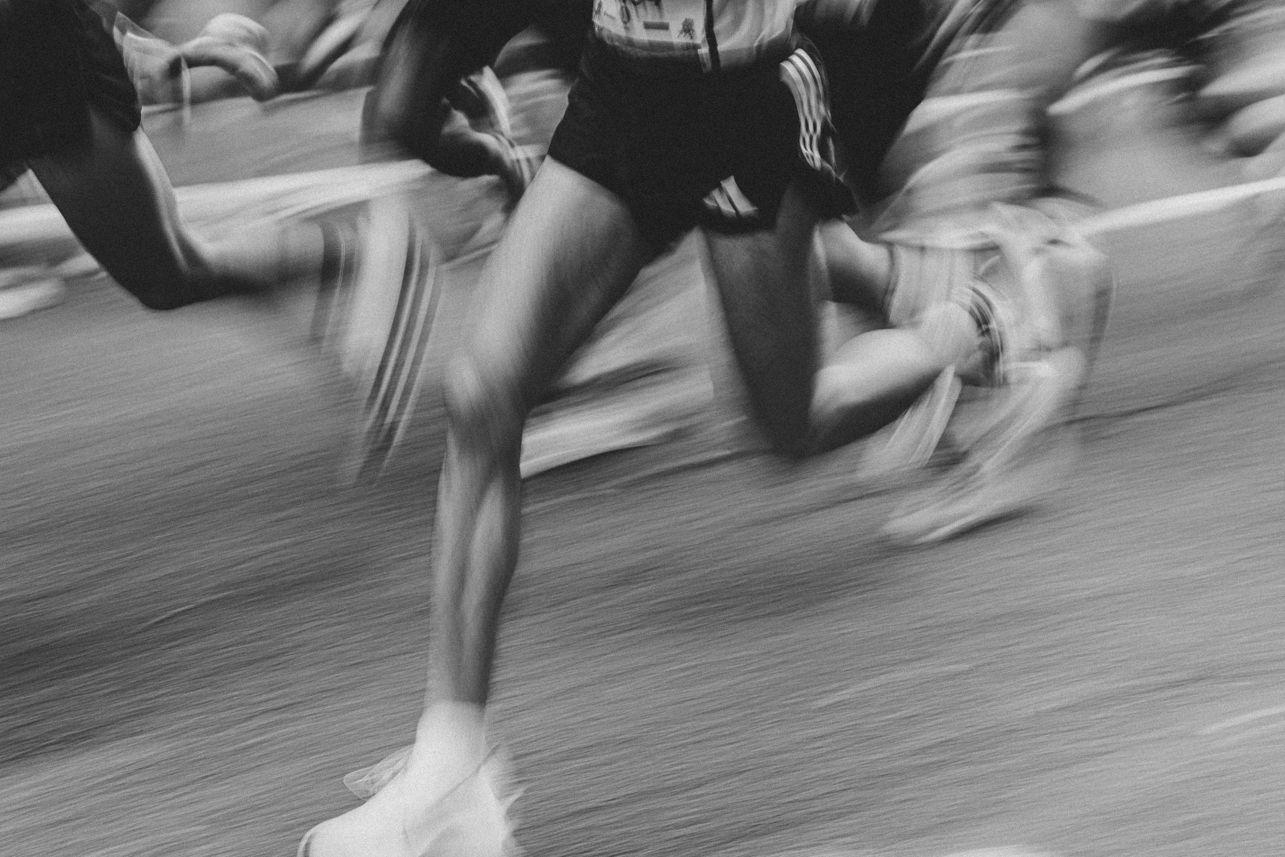 Deportistas en plena carrera, en movimiento rápido, en un evento deportivo indoor, con atletas vestidas con ropa deportiva y zapatillas.