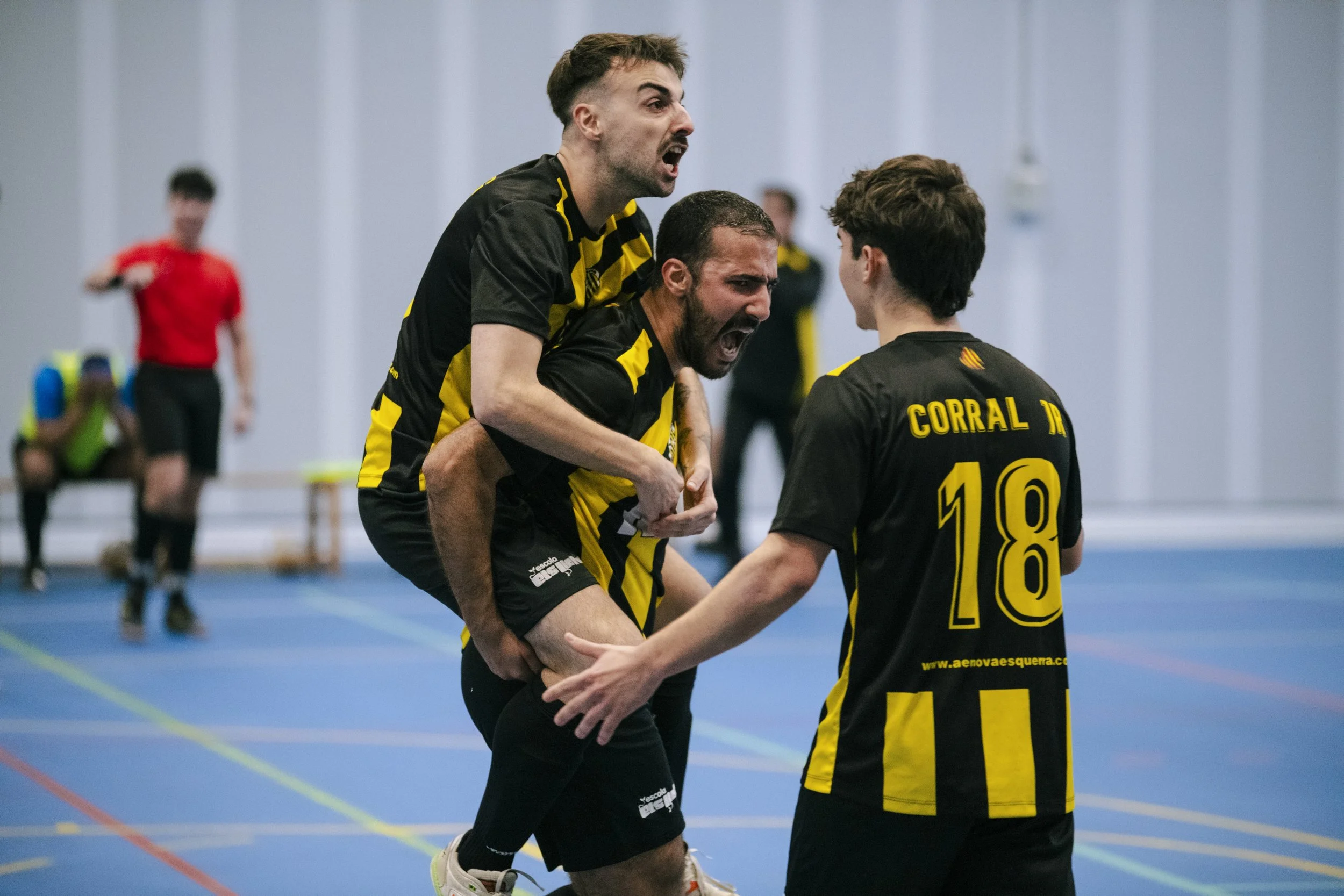 Jugadores de fútbol sala en una cancha cubierta celebrando un gol, con expresión de alegría y victoria.