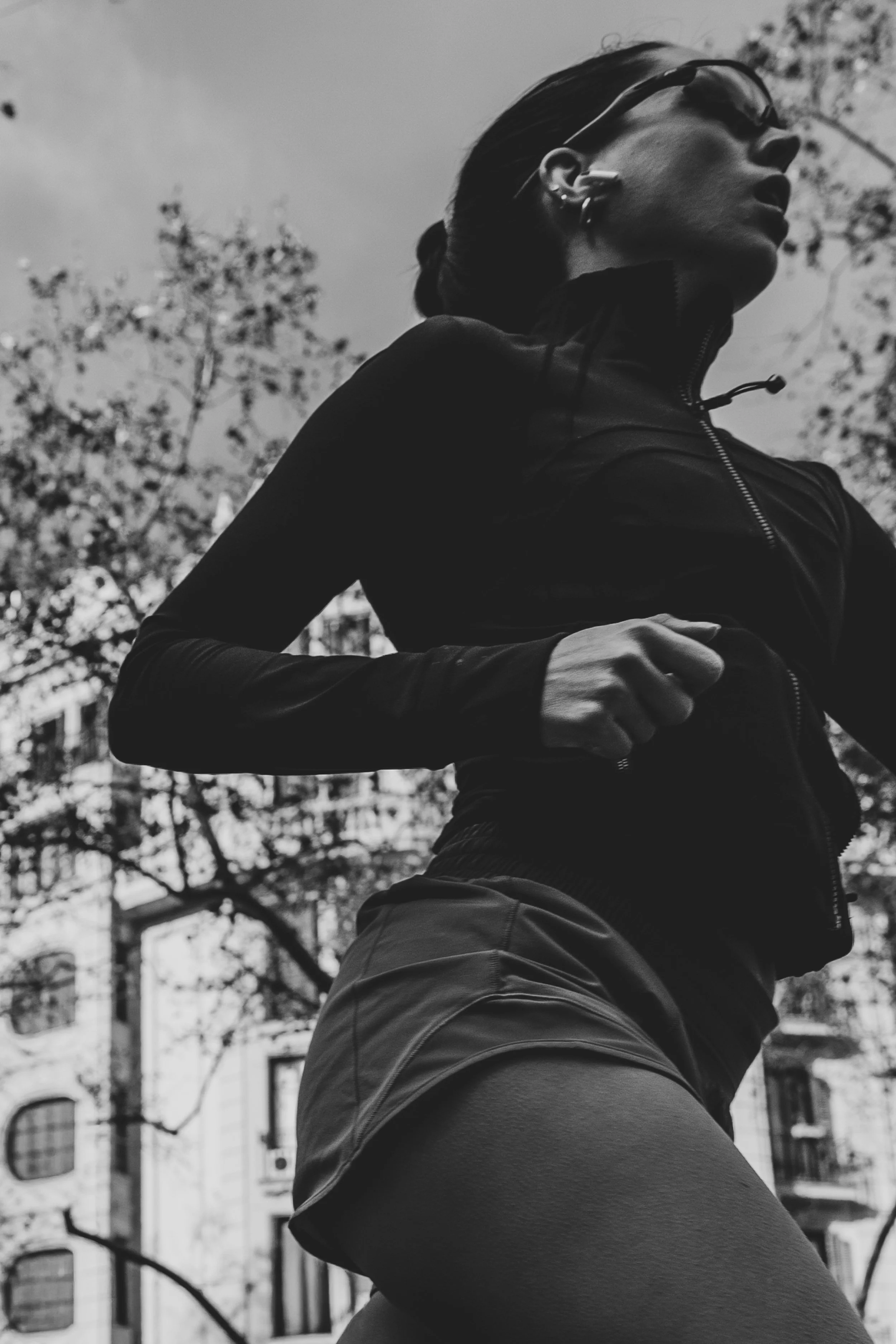 Mujer corriendo al aire libre con árboles y edificios de fondo en blanco y negro.