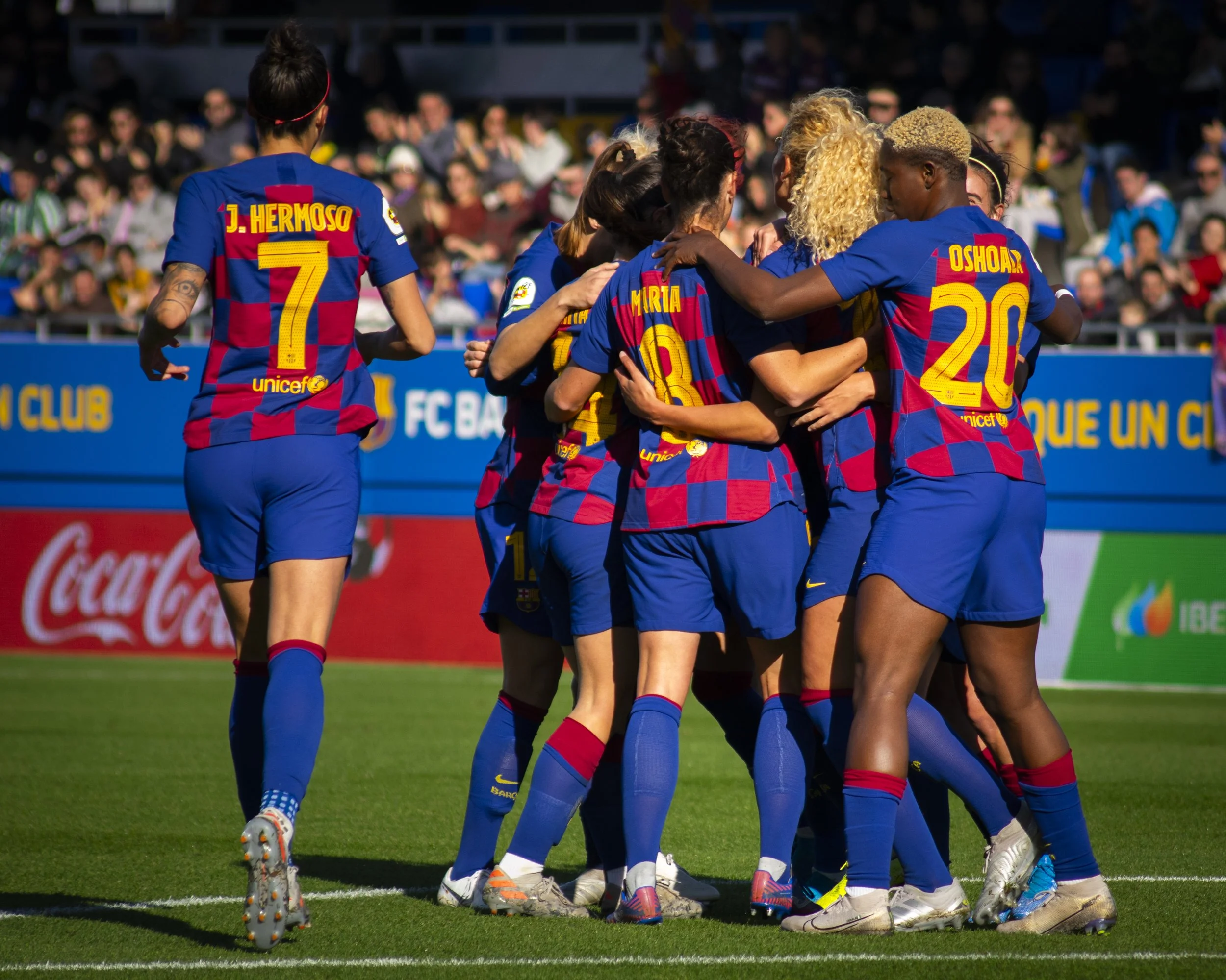 Grupo de jugadoras de fútbol en uniforme del FC Barcelona, celebrando en el campo.