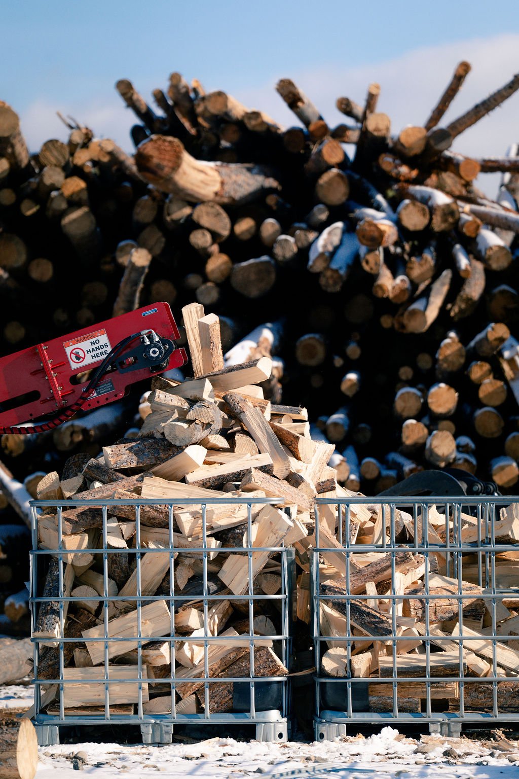 Heavy machinery slicing lumber into firewood and stacking into a metal crate.