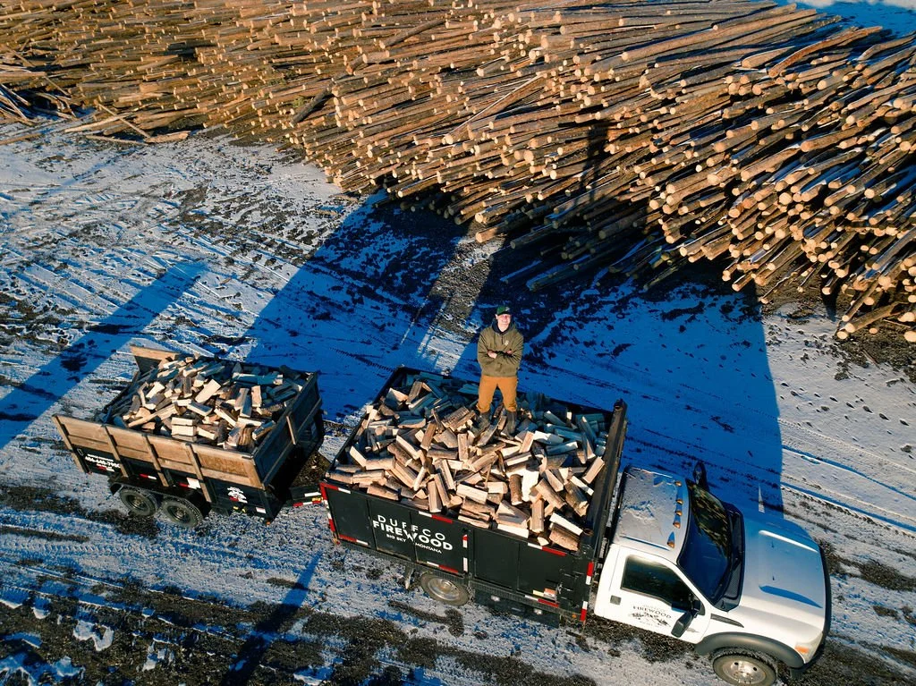 Drone footage of Duffco Firewood founder, Matt Duffy, standing on top of firewood stacked in a Duffco Firewood branded truck. 