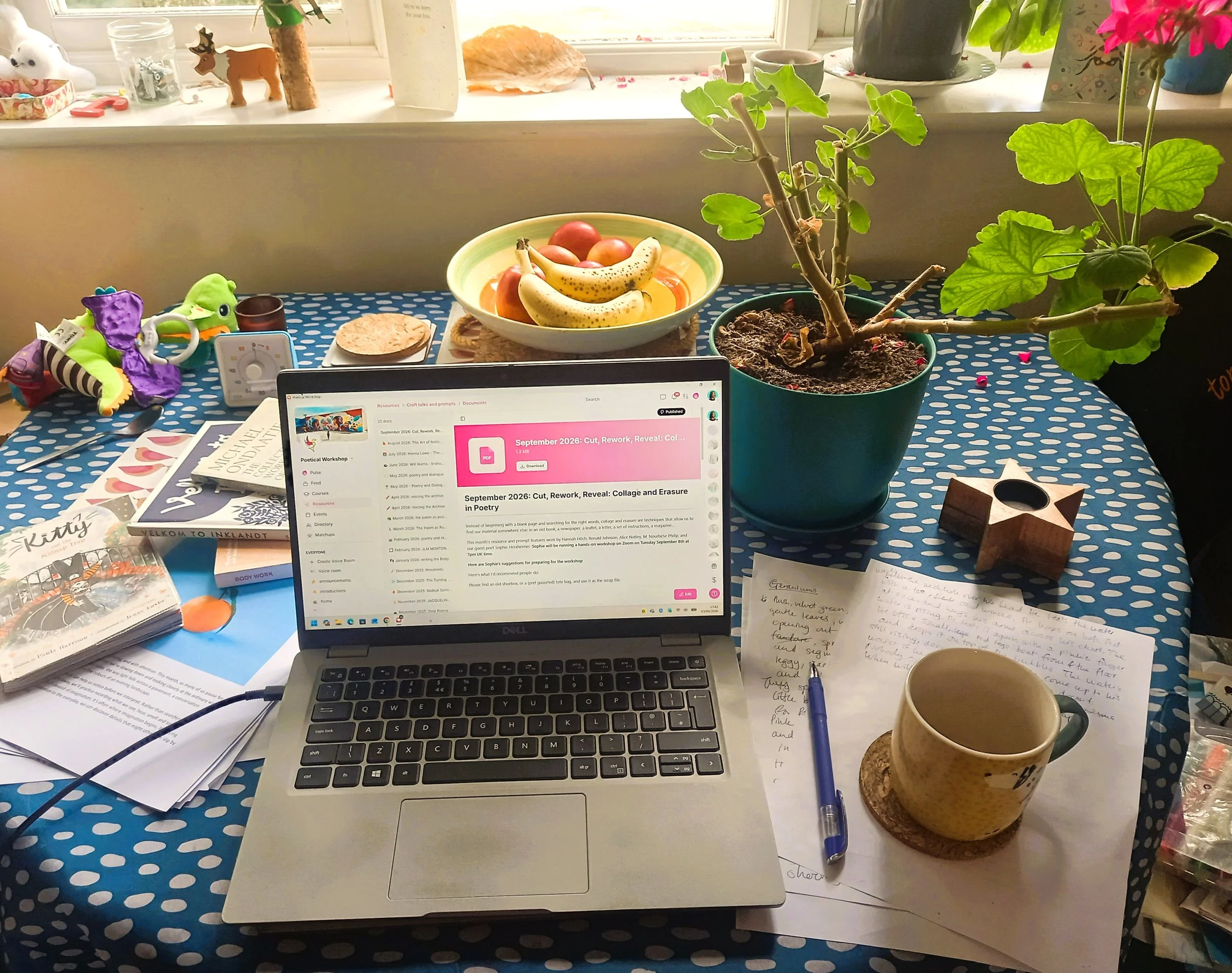 table with laptop computer, fruit bowl and assorted pens, papers and children's toys.