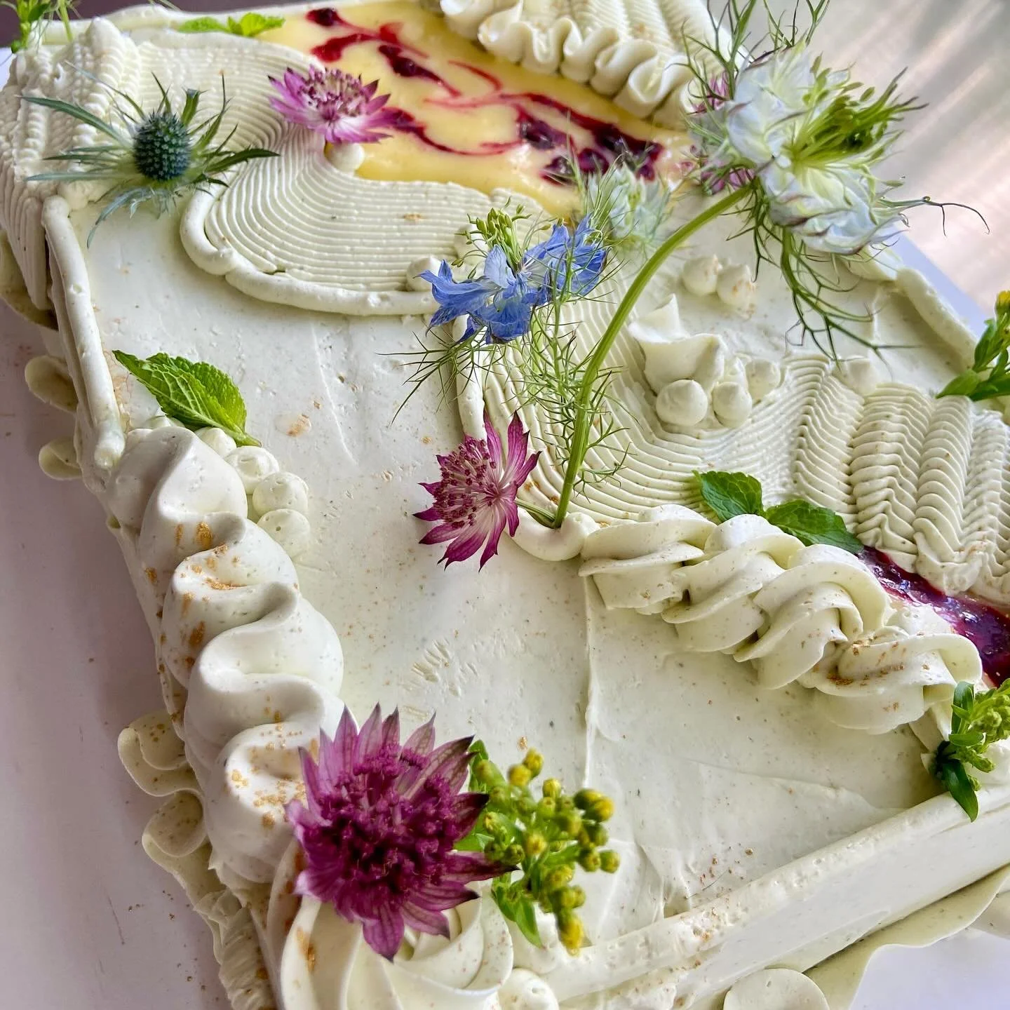 Close-up of a decorated heart-shaped cake with white icing, fresh flowers, and fruit filling visible from a slice.