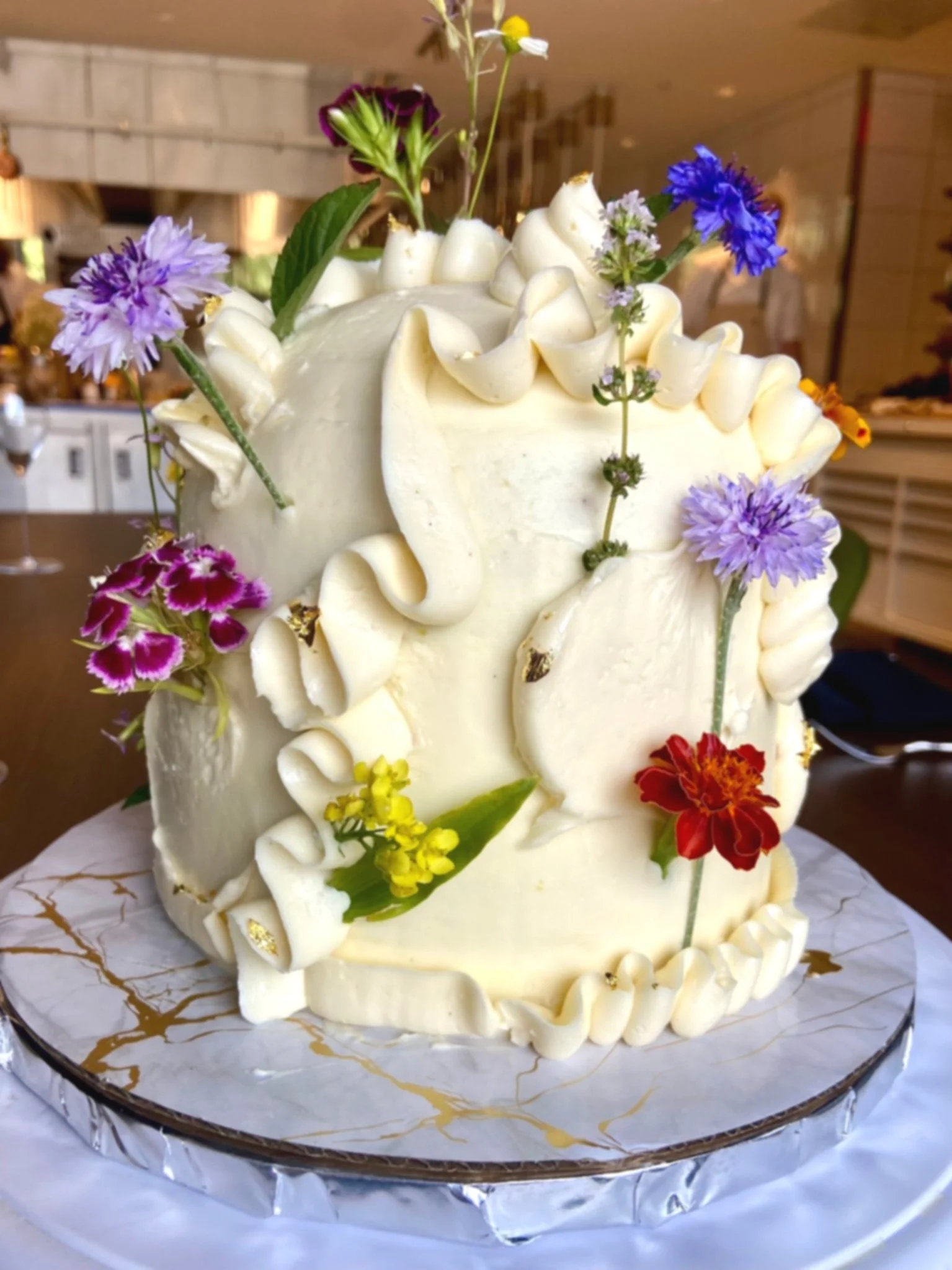 A white cake decorated with colorful flowers and floral decorations on top, placed on a marble base.