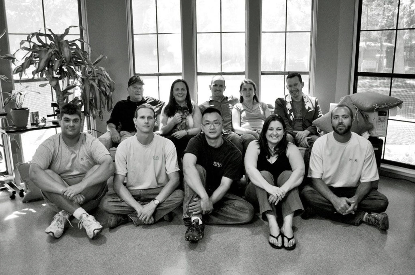 Early MAK Design + Build team gathered together indoors right after moving into downtown Davis office.  The team is seated in front of large windows.”