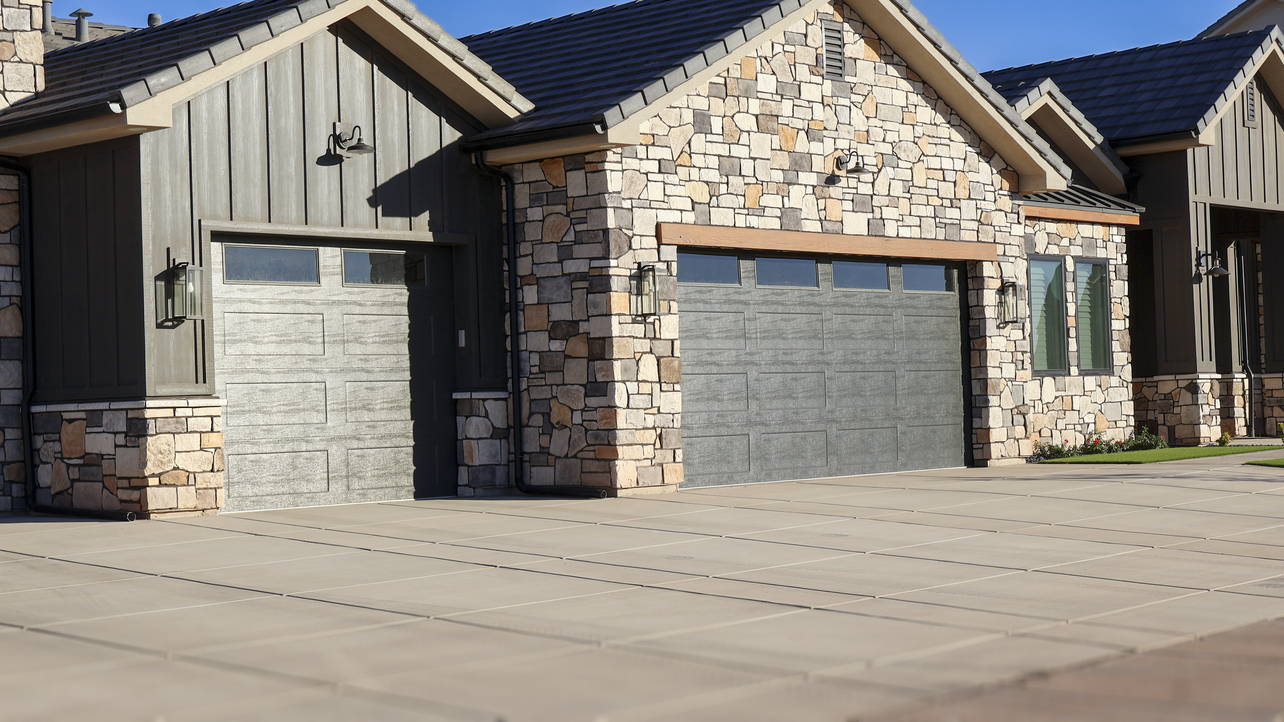 A modern house with stone and wood exterior, two garage doors, and a concrete driveway.