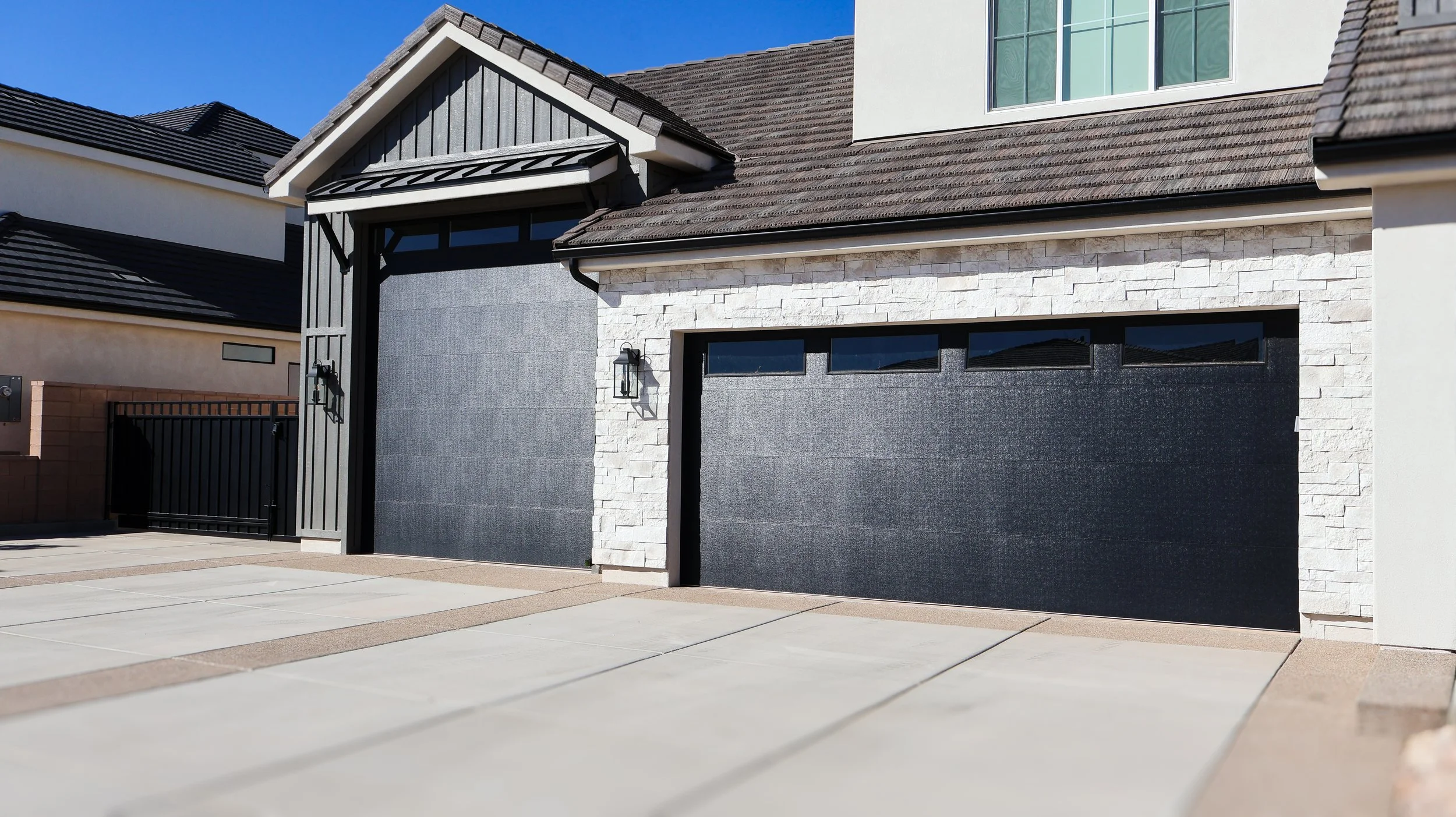 Modern house garage with black garage doors, stone accents, and exterior lighting, with a concrete driveway.
