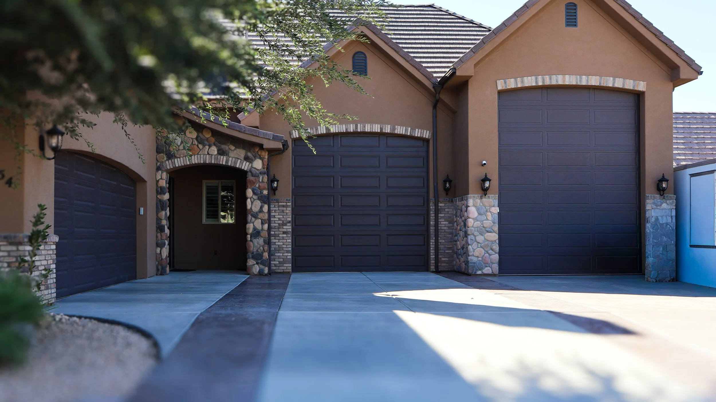 Front view of a suburban house with three closed dark garage doors, stone and brick accents, and exterior lighting fixtures
