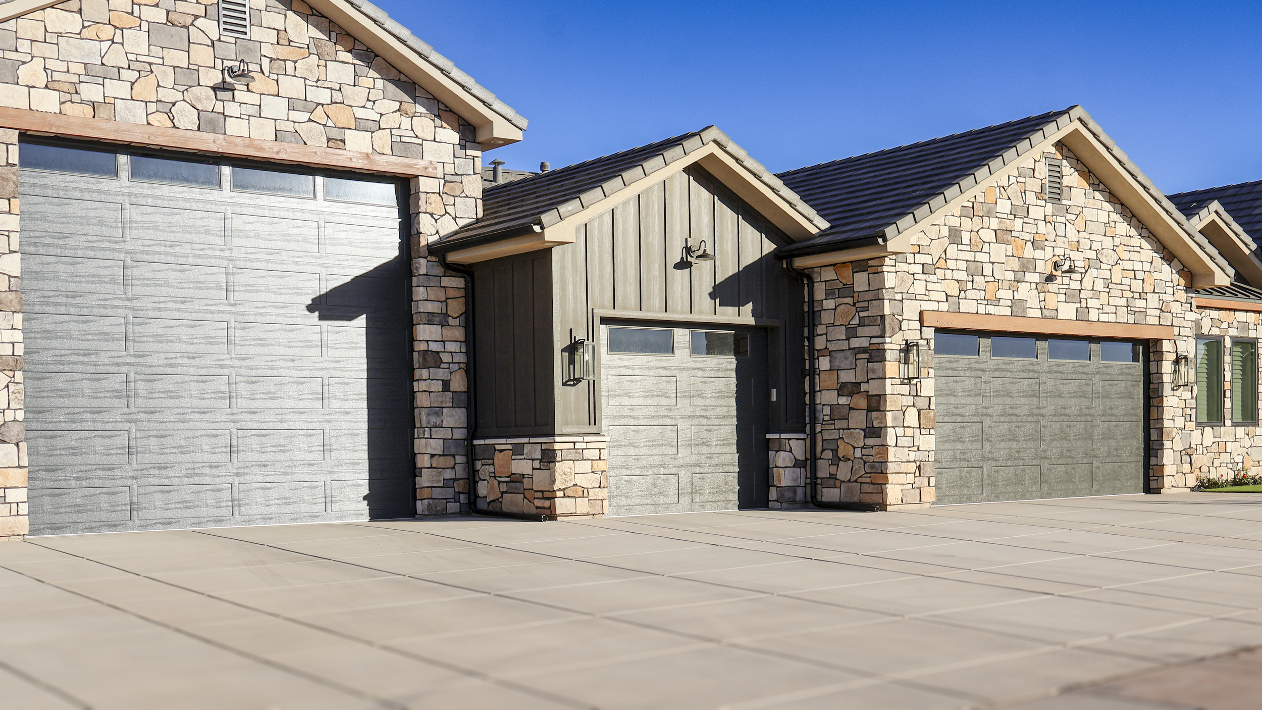 Three garage doors on a house with brick and wood siding under a clear blue sky.