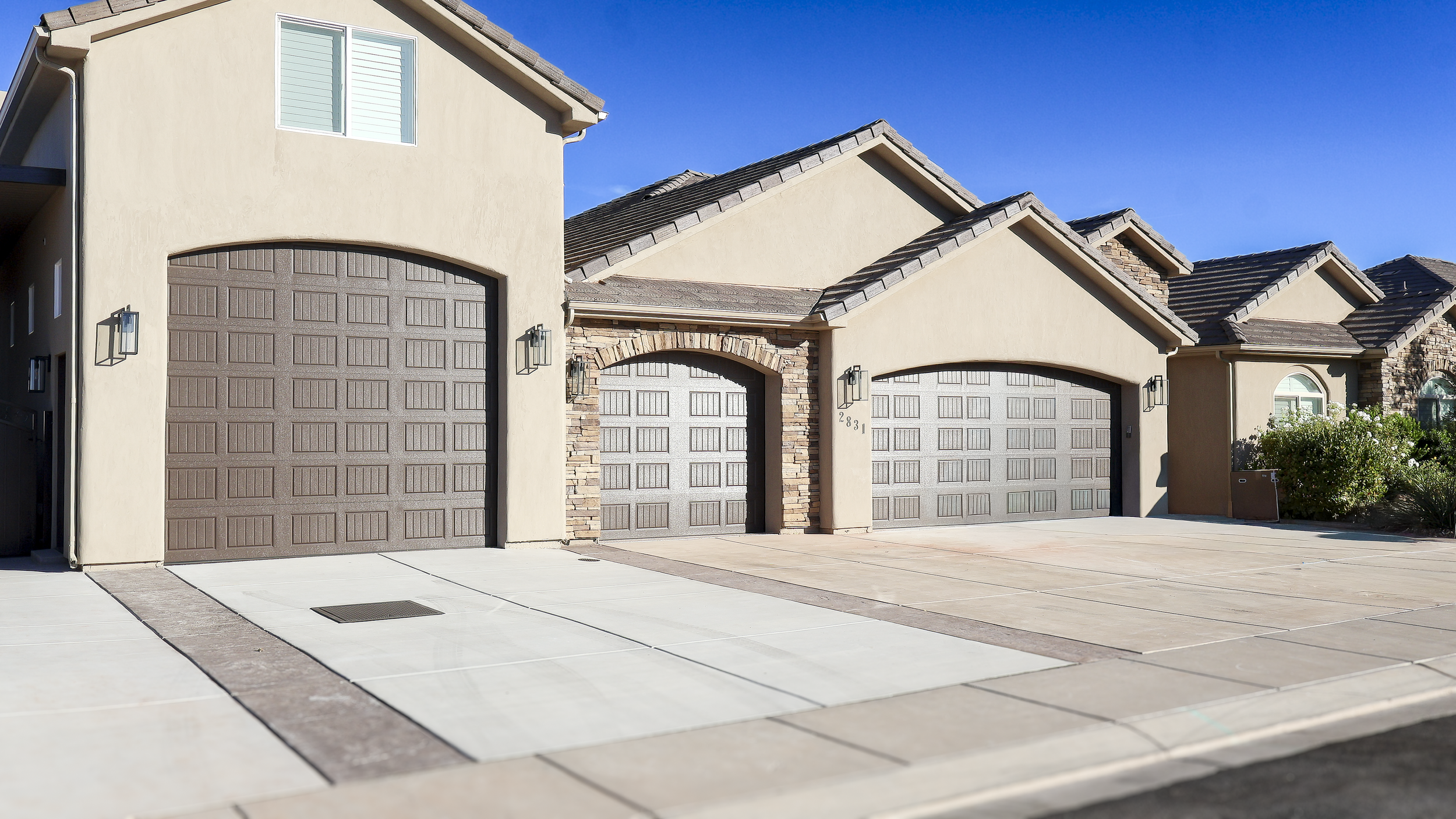 A row of attached modern houses with attached garages, light beige walls, brown garage doors, and tiled roofs, under a clear blue sky.