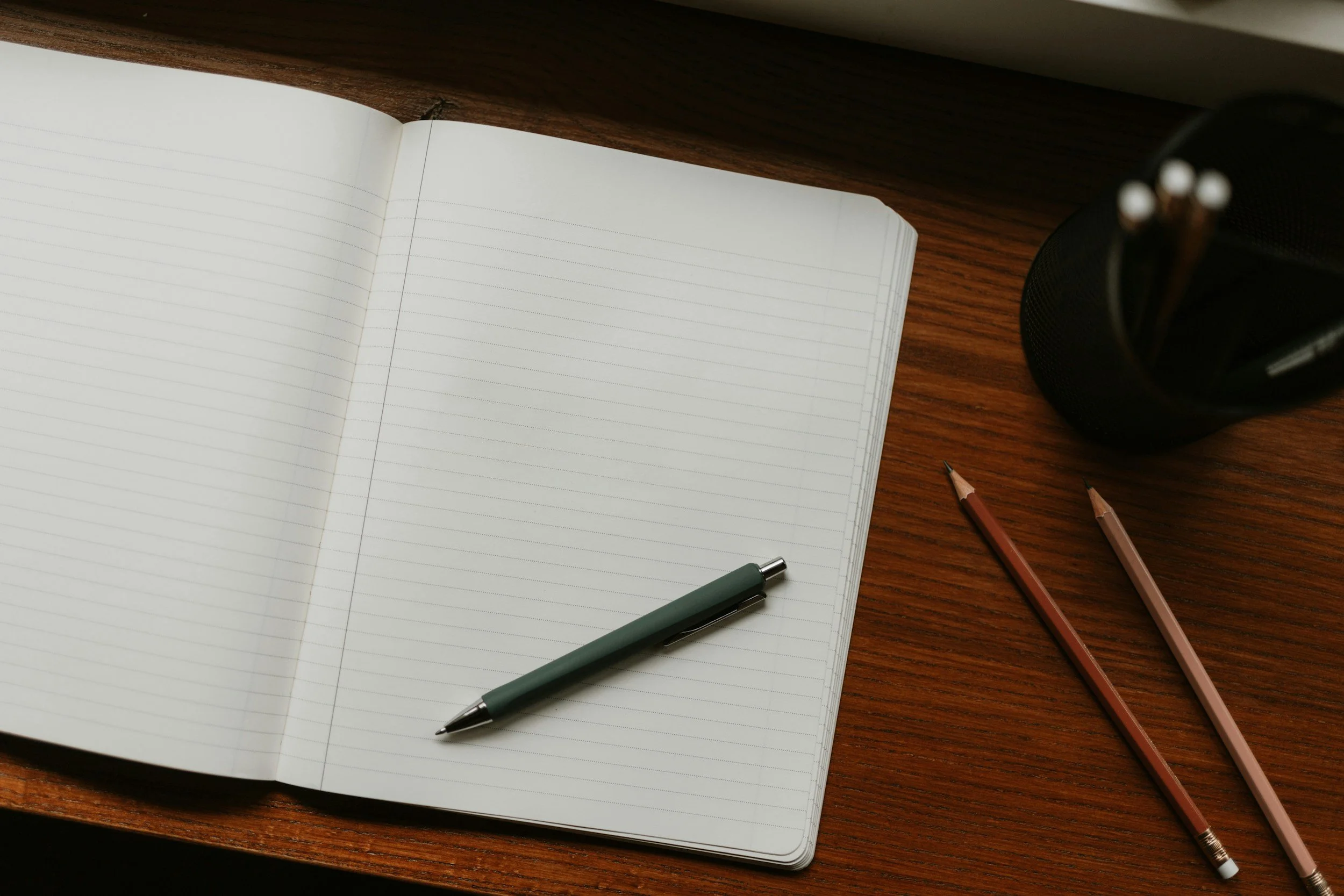 open notebook with lined-paper on a desk with pen on top