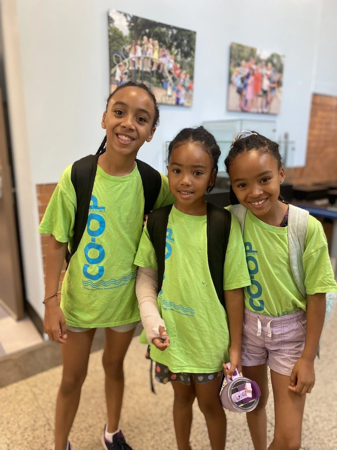 3 girls wearing Co-Op Summer Enrichment shirts posing in a classroom