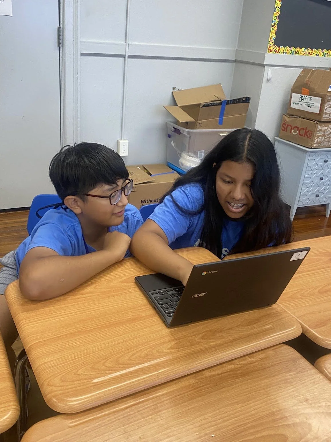 Two students in blue shirts working on a Chromebook