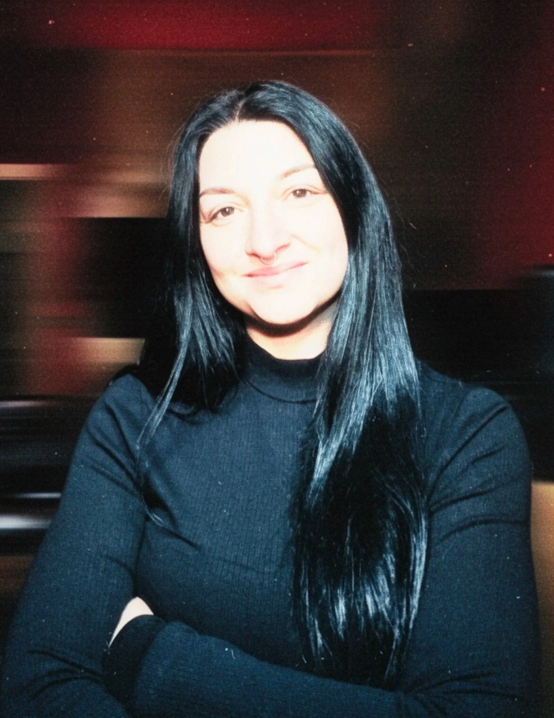 Eine Frau mit langen schwarzen Haaren trägt ein schwarzes Oberteil und lächelt in die Kamera.