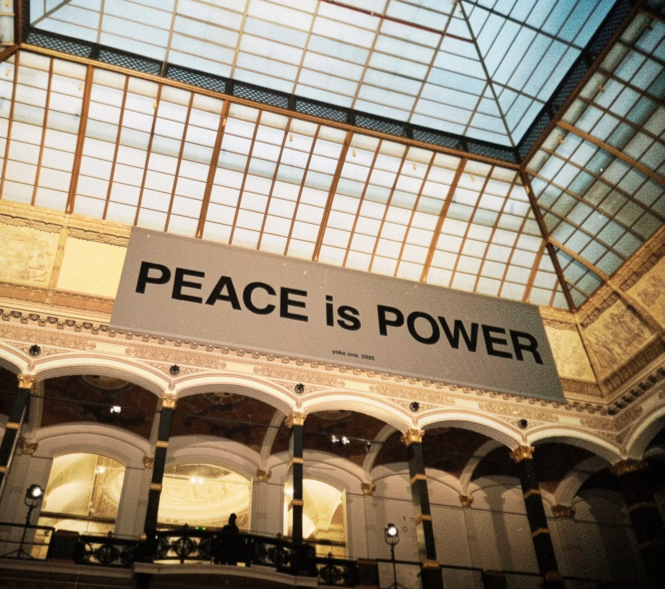 Großes Banner mit der Aufschrift »PEACE is POWER« in einem prachtvollen, historischen Gebäude mit gewölbtem Glasdach.