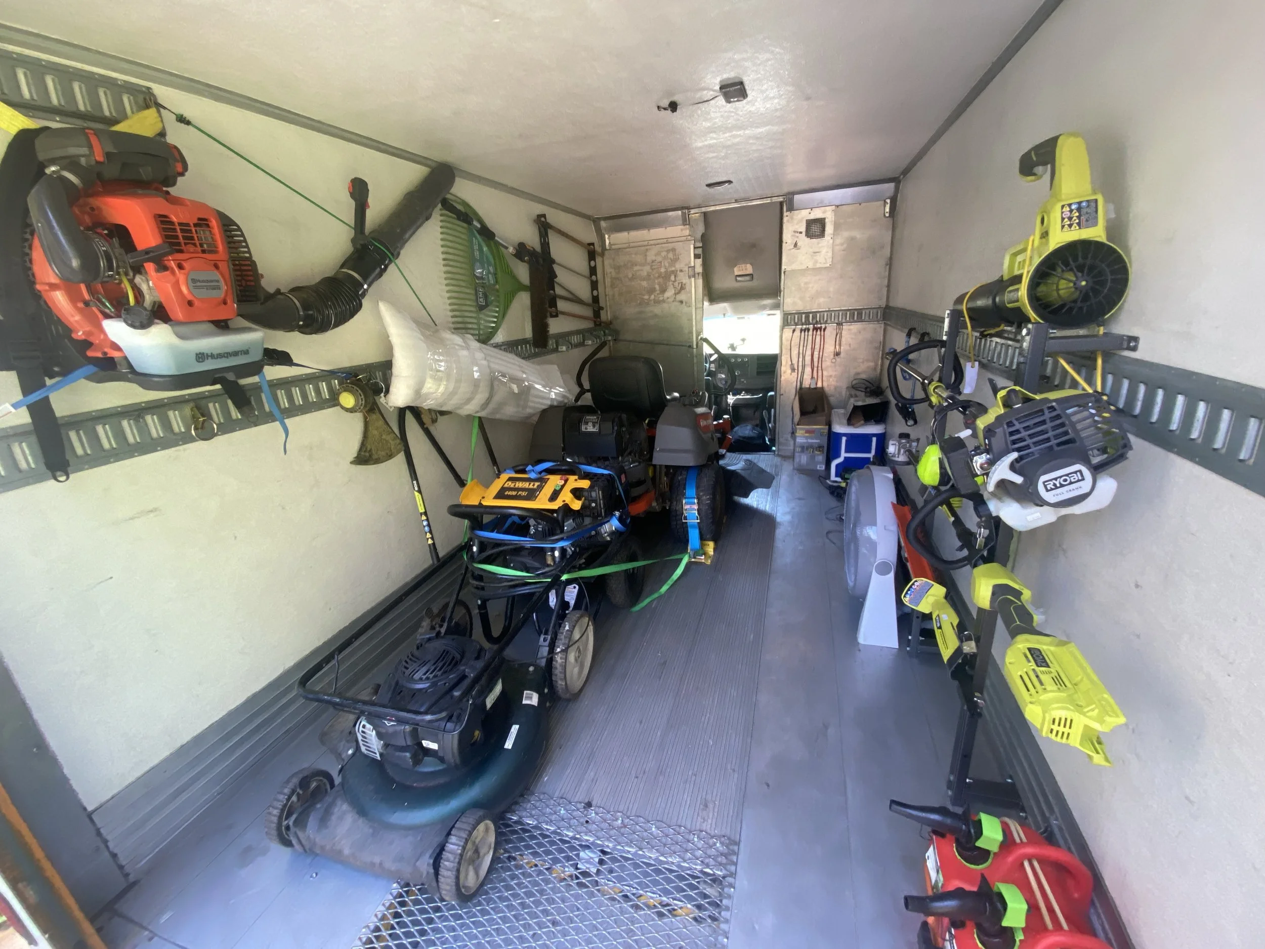 Tool storage area with various power tools and equipment, including leaf blowers, a lawnmower, and a chainsaw, organized on wall-mounted racks.