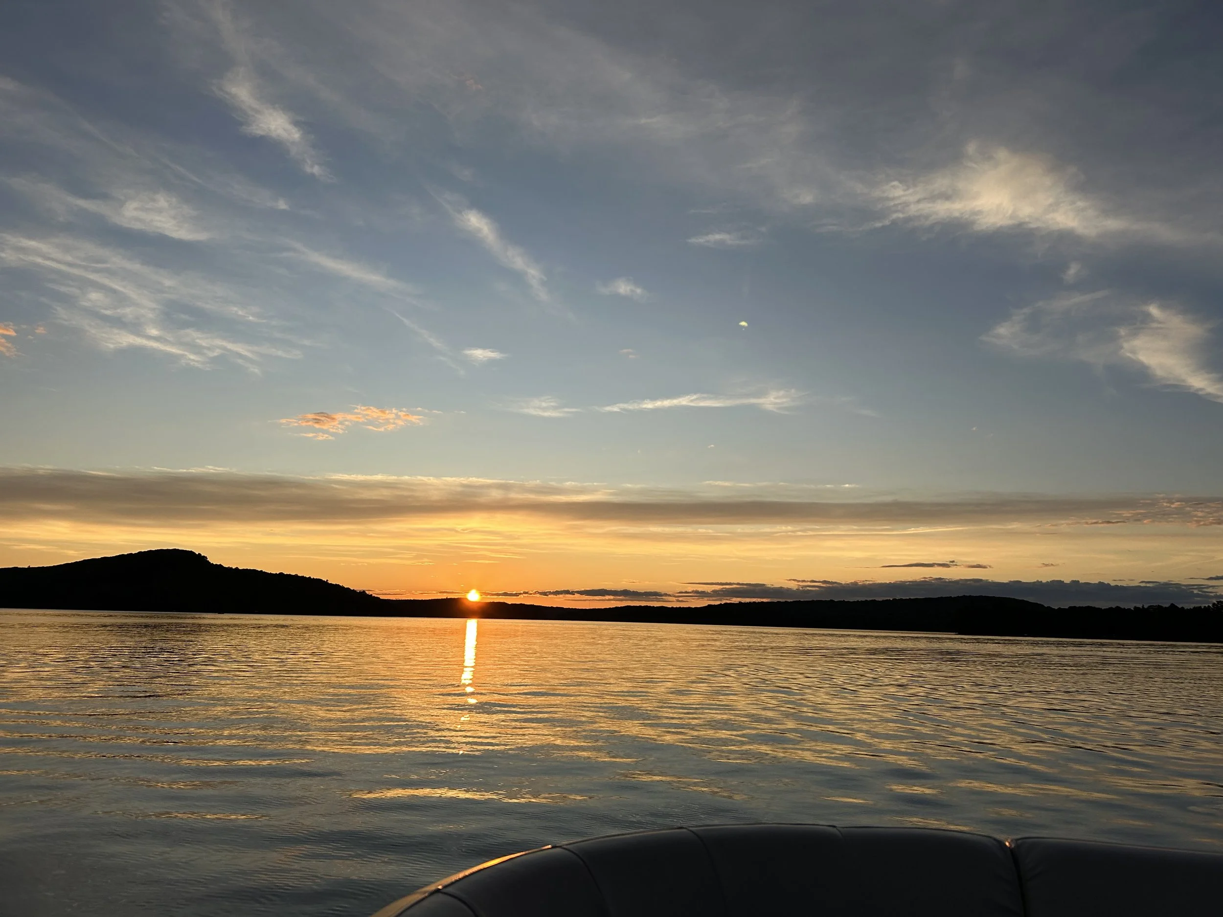 Sunset over a lake with a mountain silhouette on the horizon, reflecting golden and blue hues in the water under a partly cloudy sky.