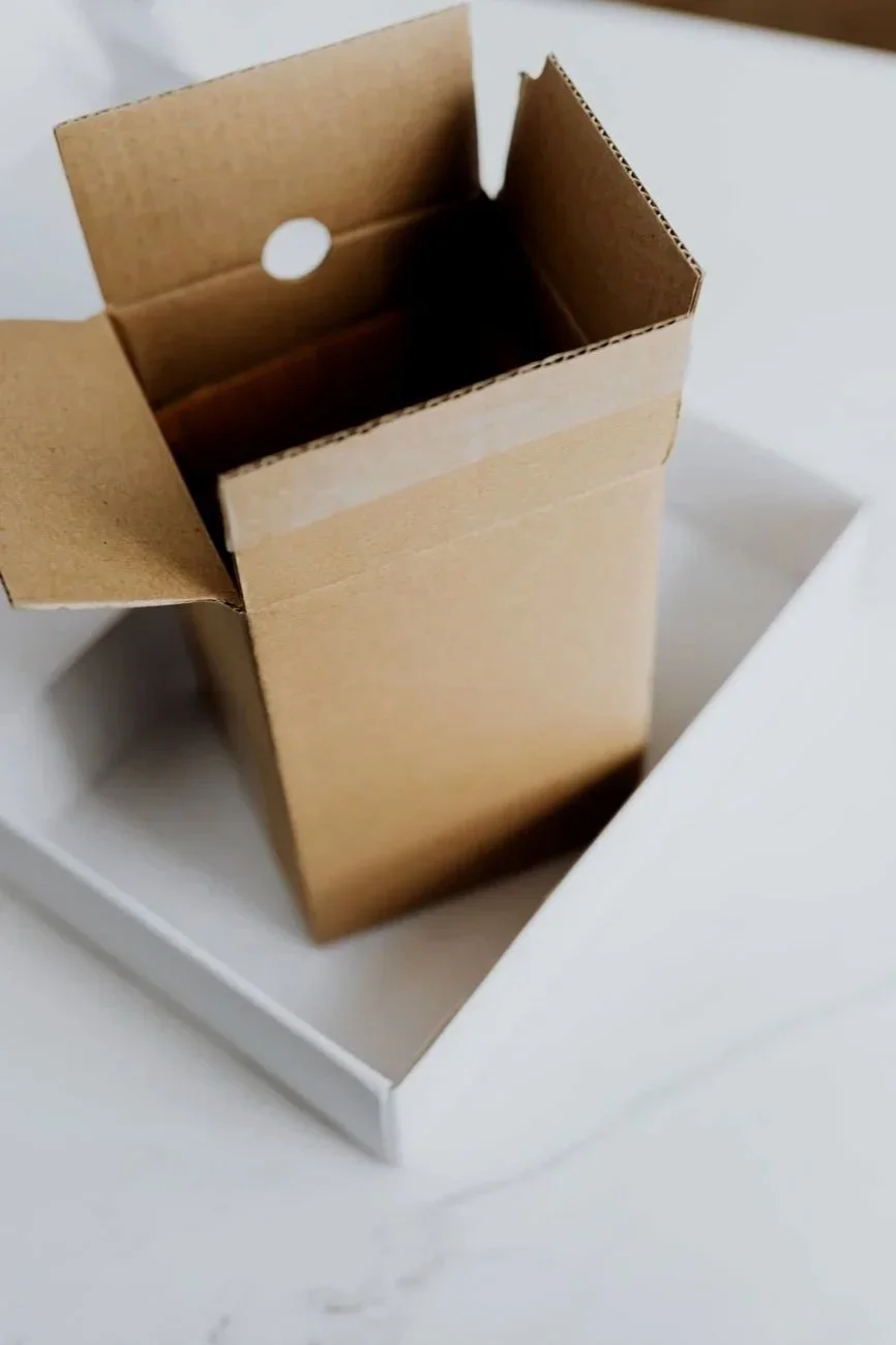 Open cardboard box inside a white packaging container on a white surface.