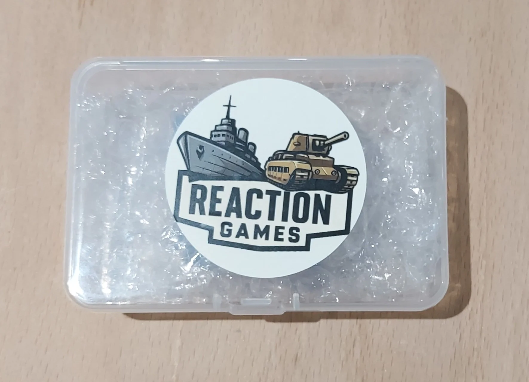 Clear plastic case with bubble wrap inside, featuring a sticker with a navy ship, a tank, and the words 'Reaction Games'.