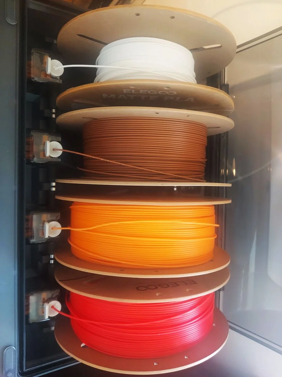 Colorful spools of filament for 3D printing, arranged on a circular rack.
