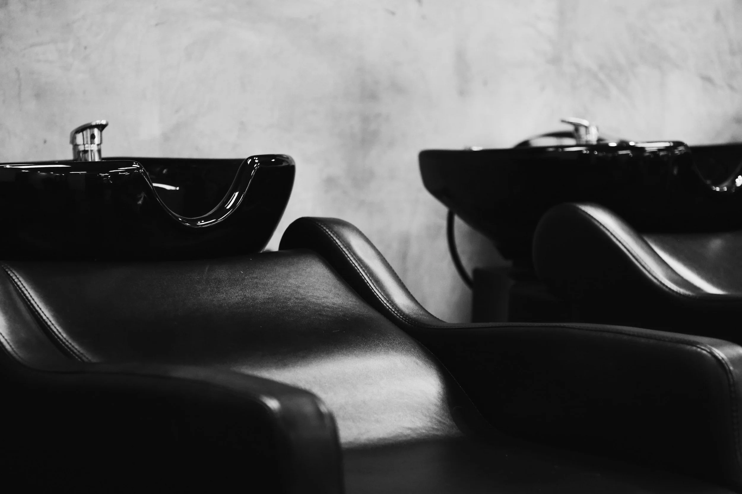 Two black salon shampoo bowls with leather chairs in a hair salon, black and white photo.
