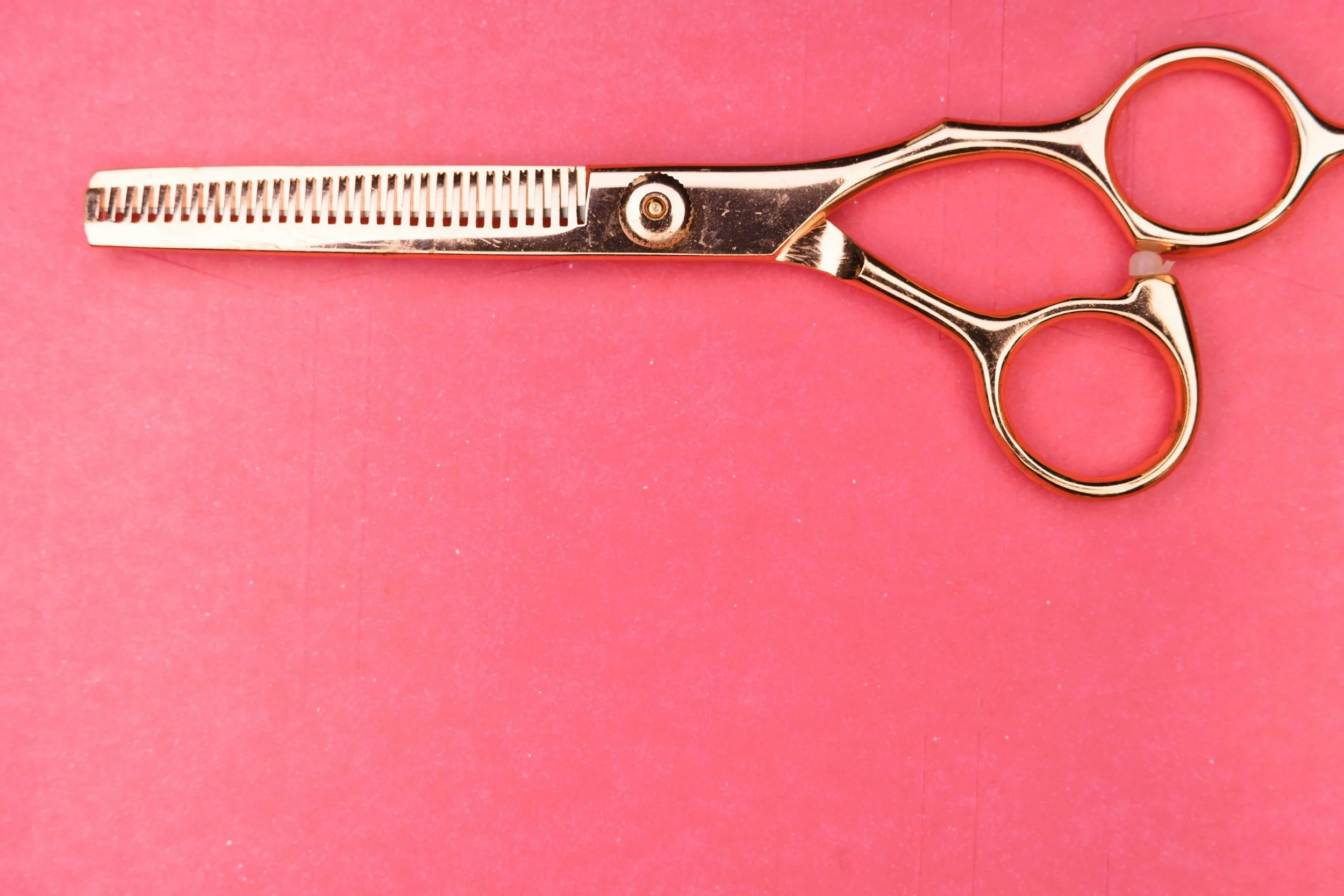 A pair of medical scissors with a shiny metallic finish, placed on a pink background.