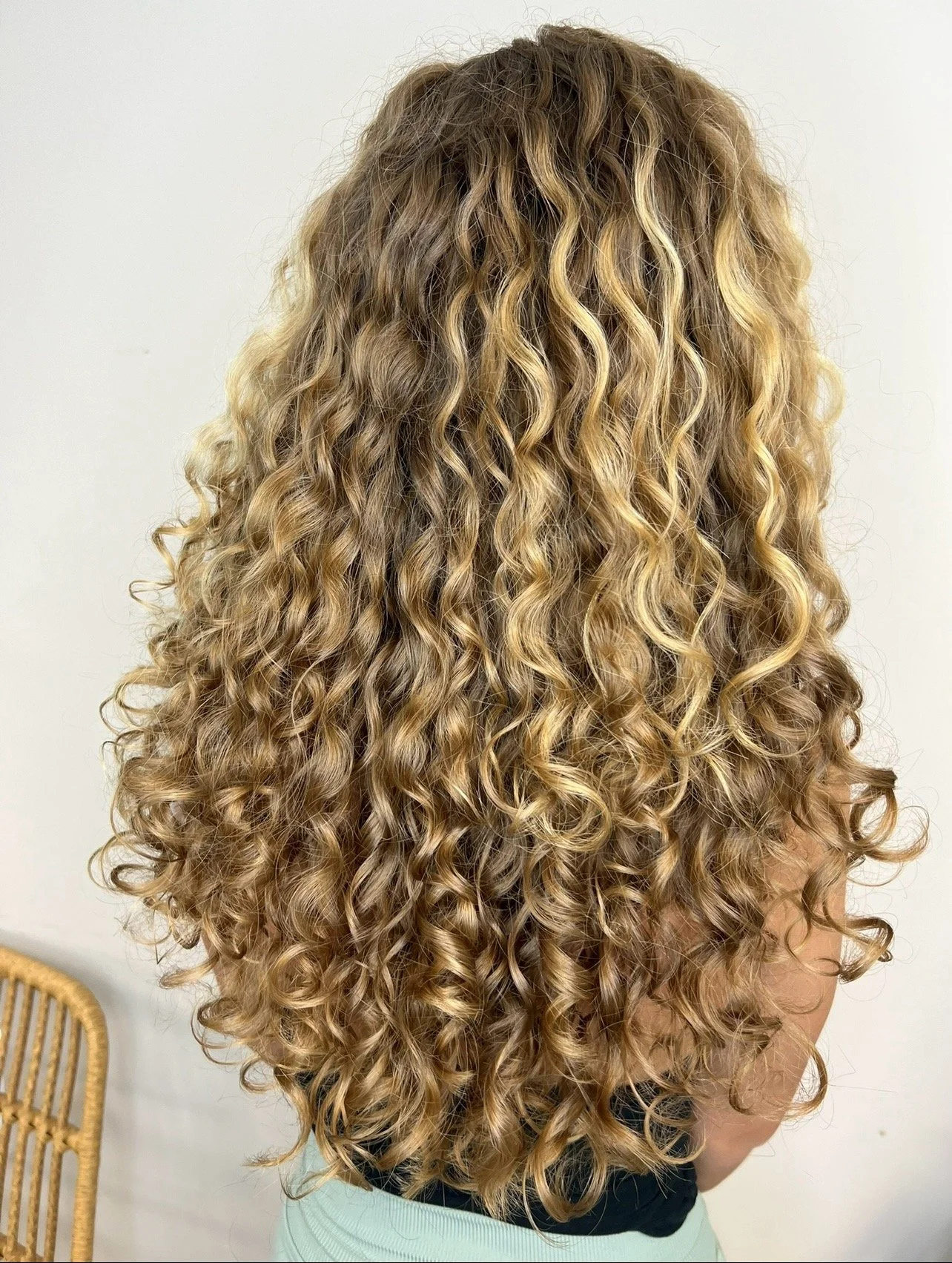 Back view of a person with long, curly, blonde hair.