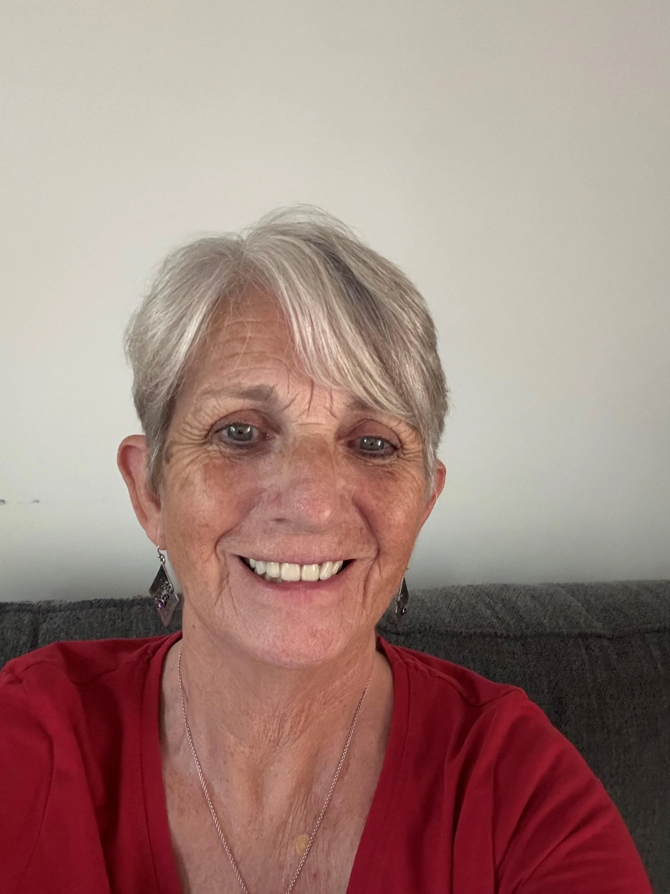 Older woman in red shirt with grey hair and wearing earrings.