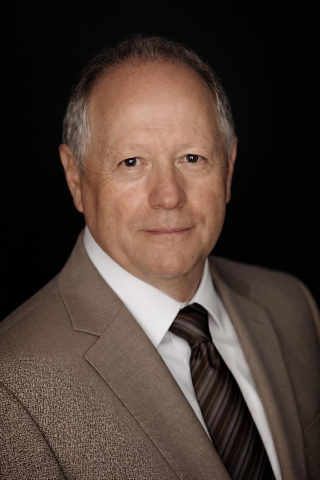 Frank Rott, director of board, he has short gray hair, and a serious expression, dressed in a gray checkered blazer, white shirt, and purple and black striped tie.