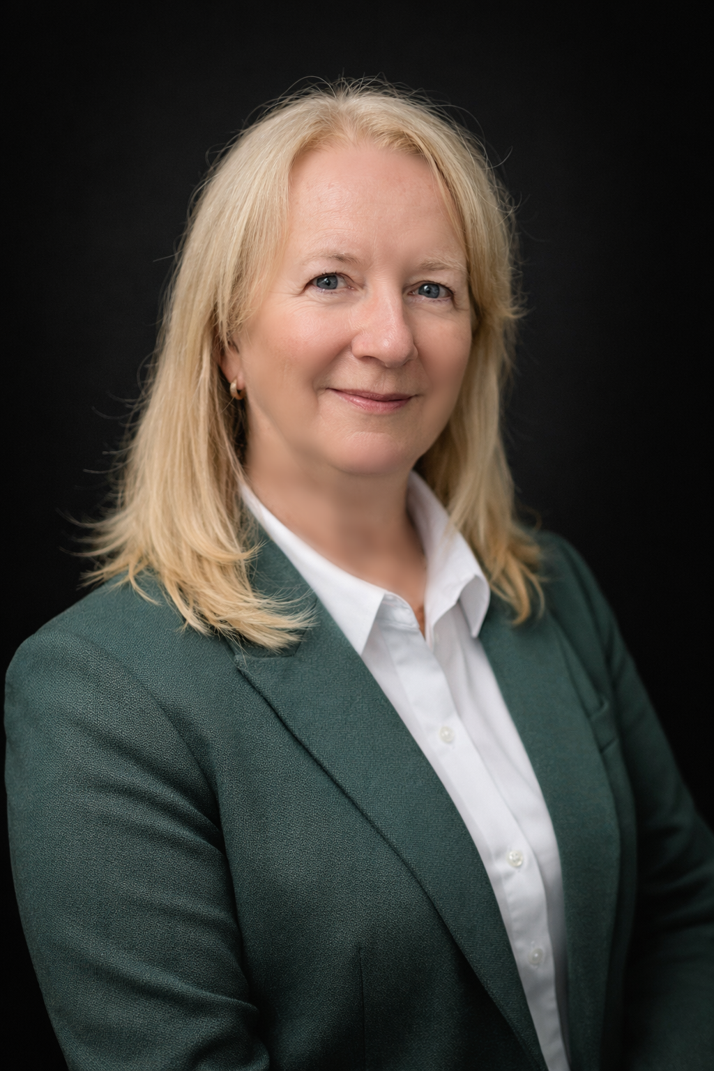 Rhona Guertin, treasurer, senior woman with shoulder-length blond hair smiling, wearing a floral blouse and a dark green blazer, seated indoors in an office or conference setting.