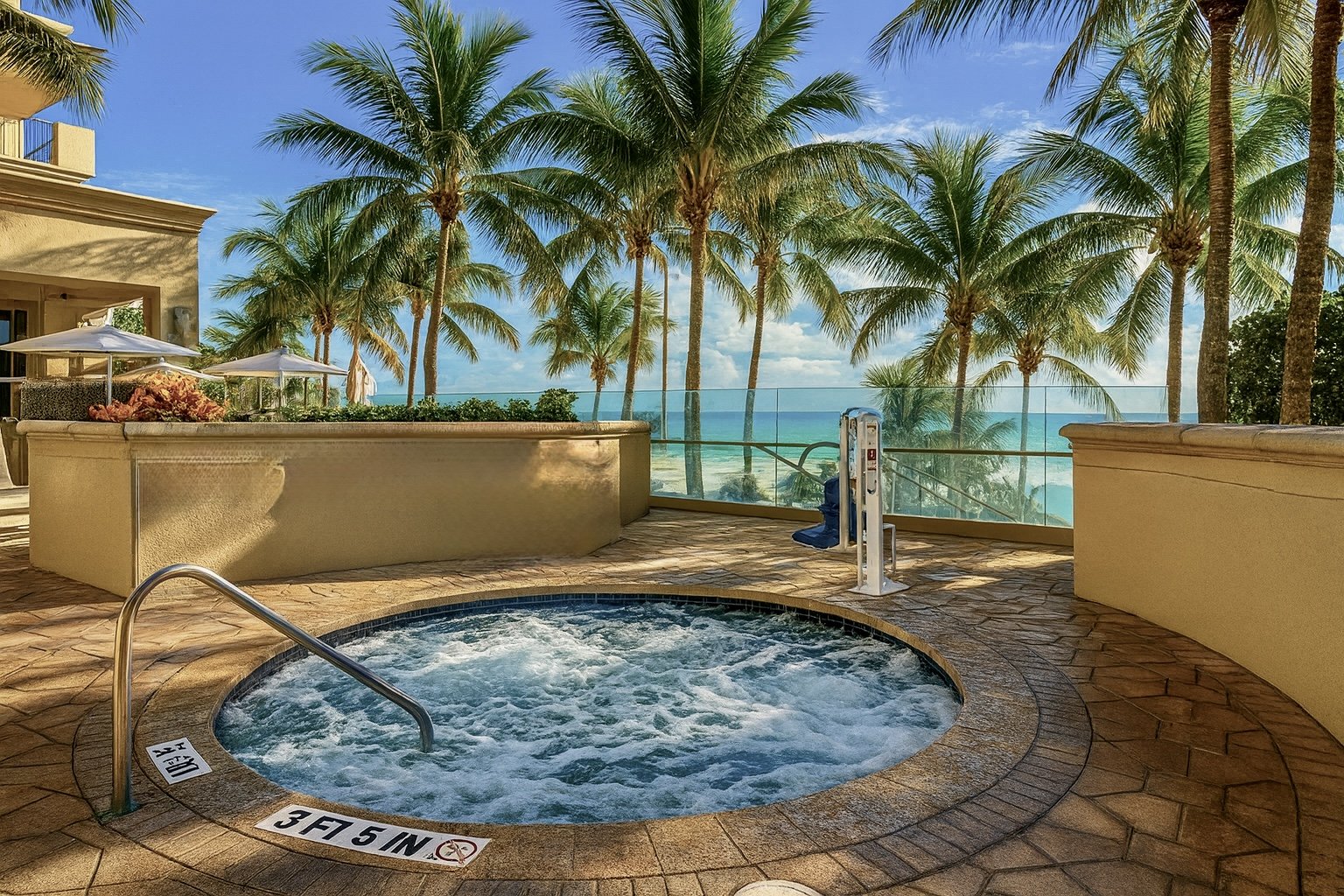 A round hot tub with clear water, metal handrail, and safety signs indicating depth at 3 feet 5 inches and 1 meter, surrounded by palm trees at a pool area on a sunny day.