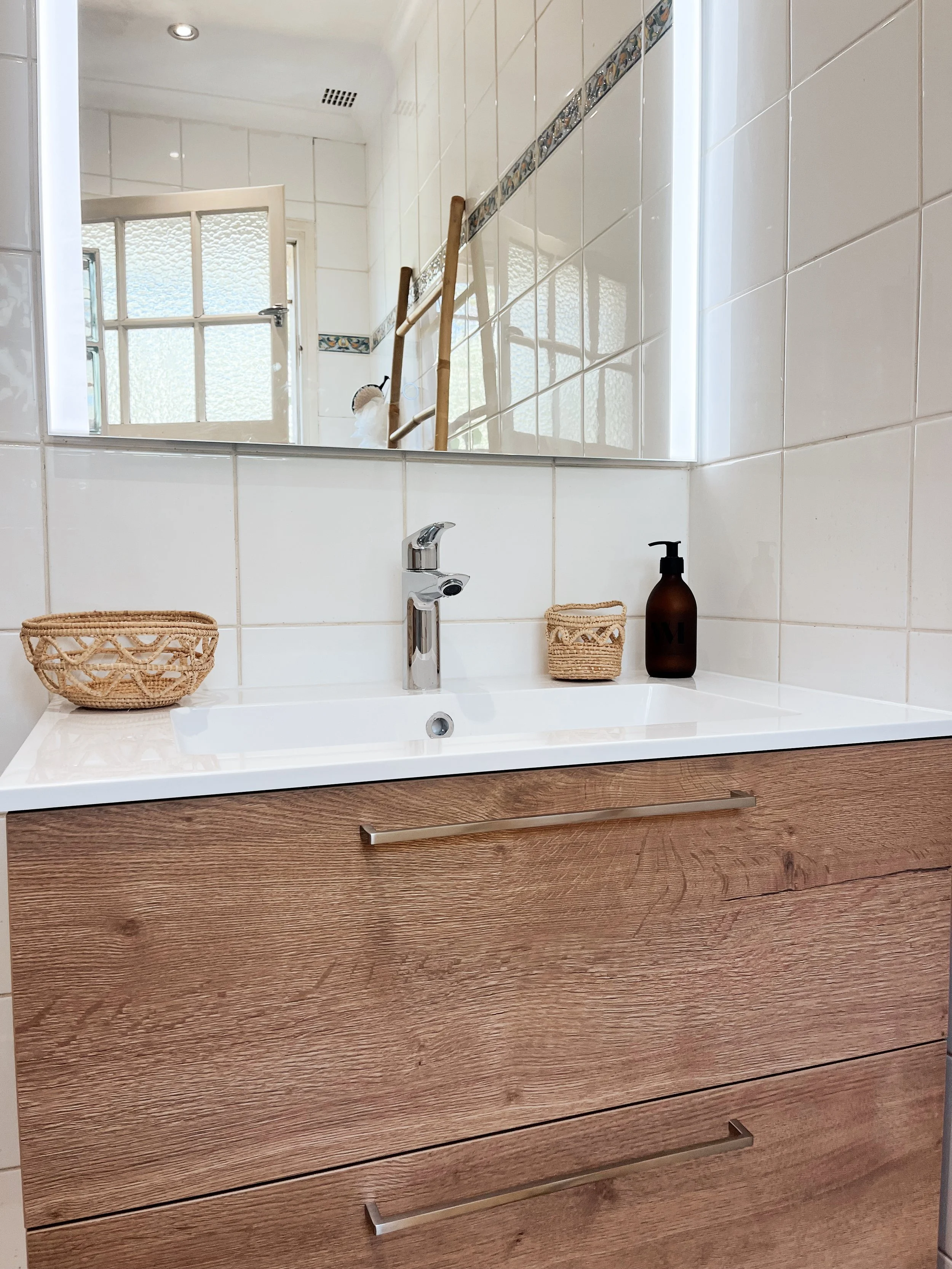 Un lavabo avec un miroir au-dessus, deux paniers en osier et un flacon de savon à main dans une salle de bain.
