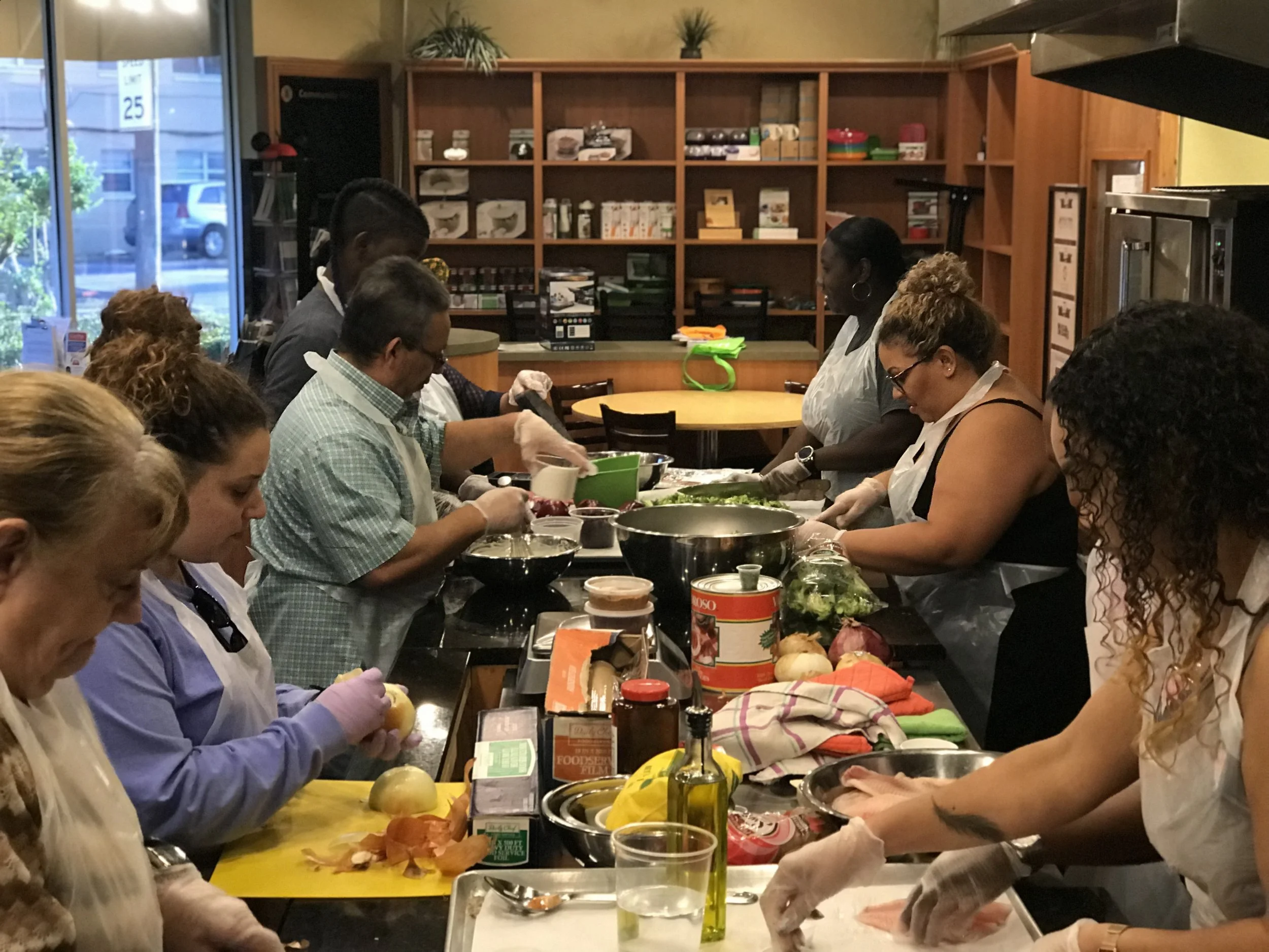 Group of people cooking together in a kitchen class, preparing food at a long counter.